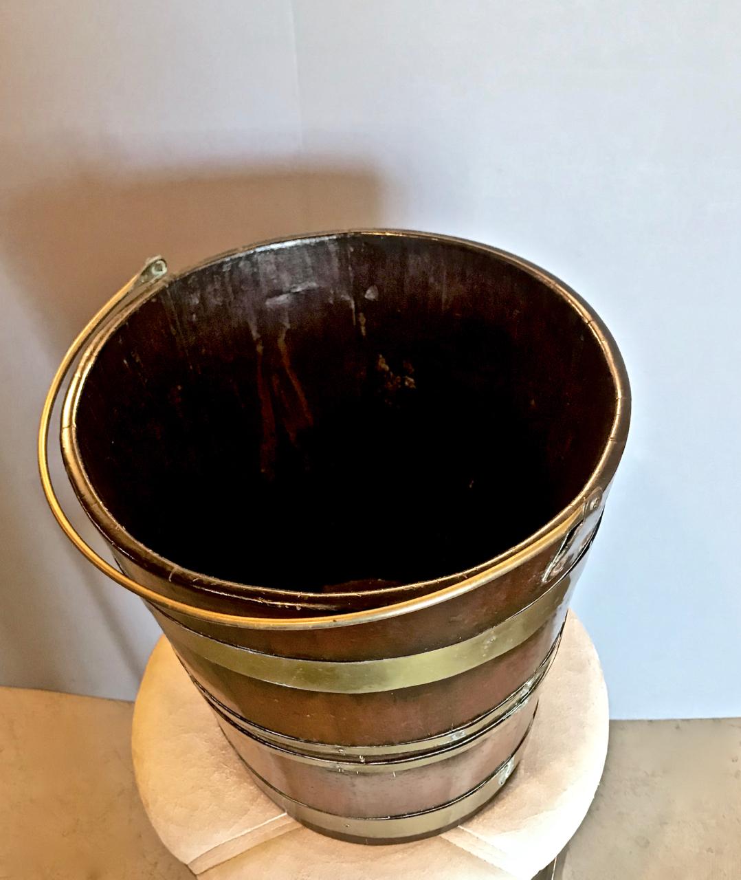 This is a classic mahogany peat bucket that is detailed with a brass handle and banding that dates to circa 1820-1830.