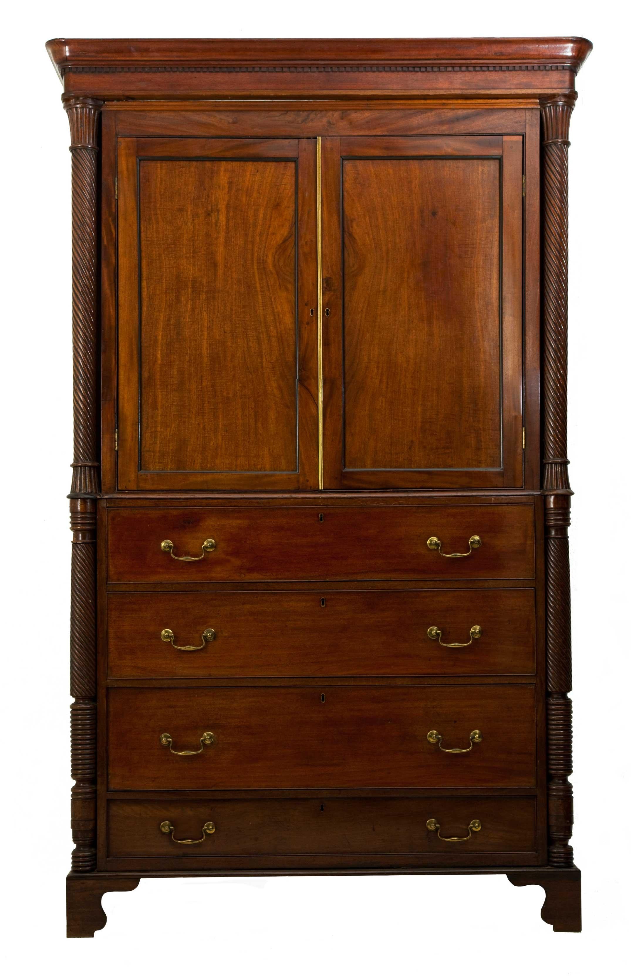 Regency mahogany press cupboard, circa 1810.
Rounded cornice with dental frieze beneath, two brass beaded cupboard doors opening to show removable linen shelves, both flanked by twisted columns.
The bottom with four assorted drawers both flanked