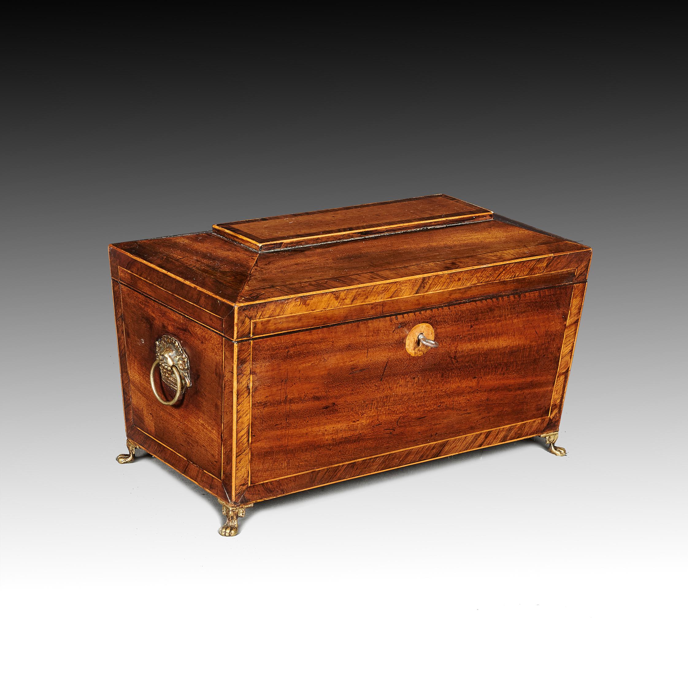 A late Regency George IV mahogany sarcophagus shaped tea caddy with boxwood stringing and rosewood banding.

English circa 1825.

The hinged top with working key opens to reveal three lidded compartment with original brass fruit basket handles