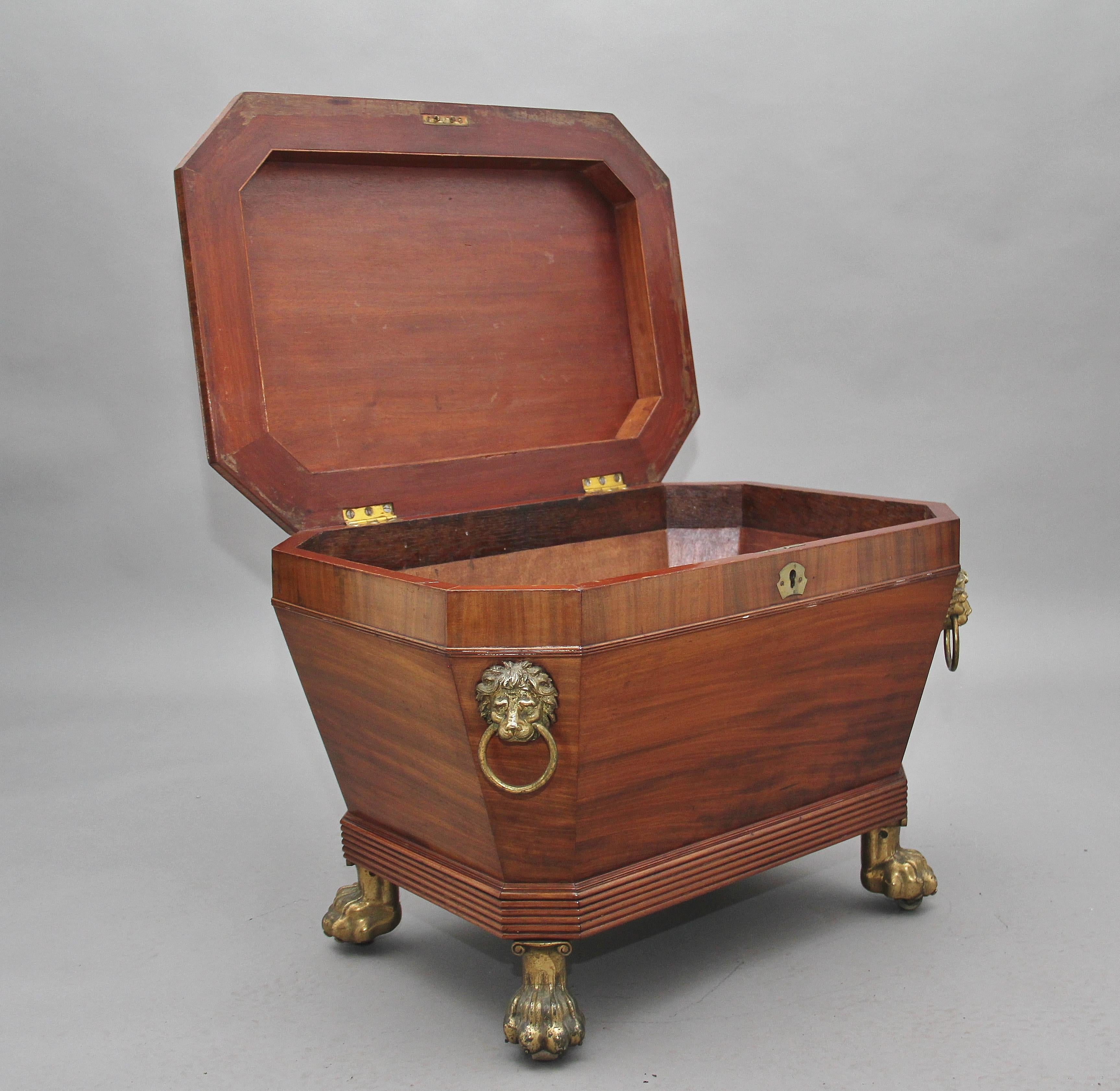 A superb quality Regency mahogany sarcophagus wine cooler, having a lovely figured top which is decorated with ebony inlay, bold brass lion mask handles to the sides, a reeded apron at the bottom of the cooler and standing on brass lion paw feet.