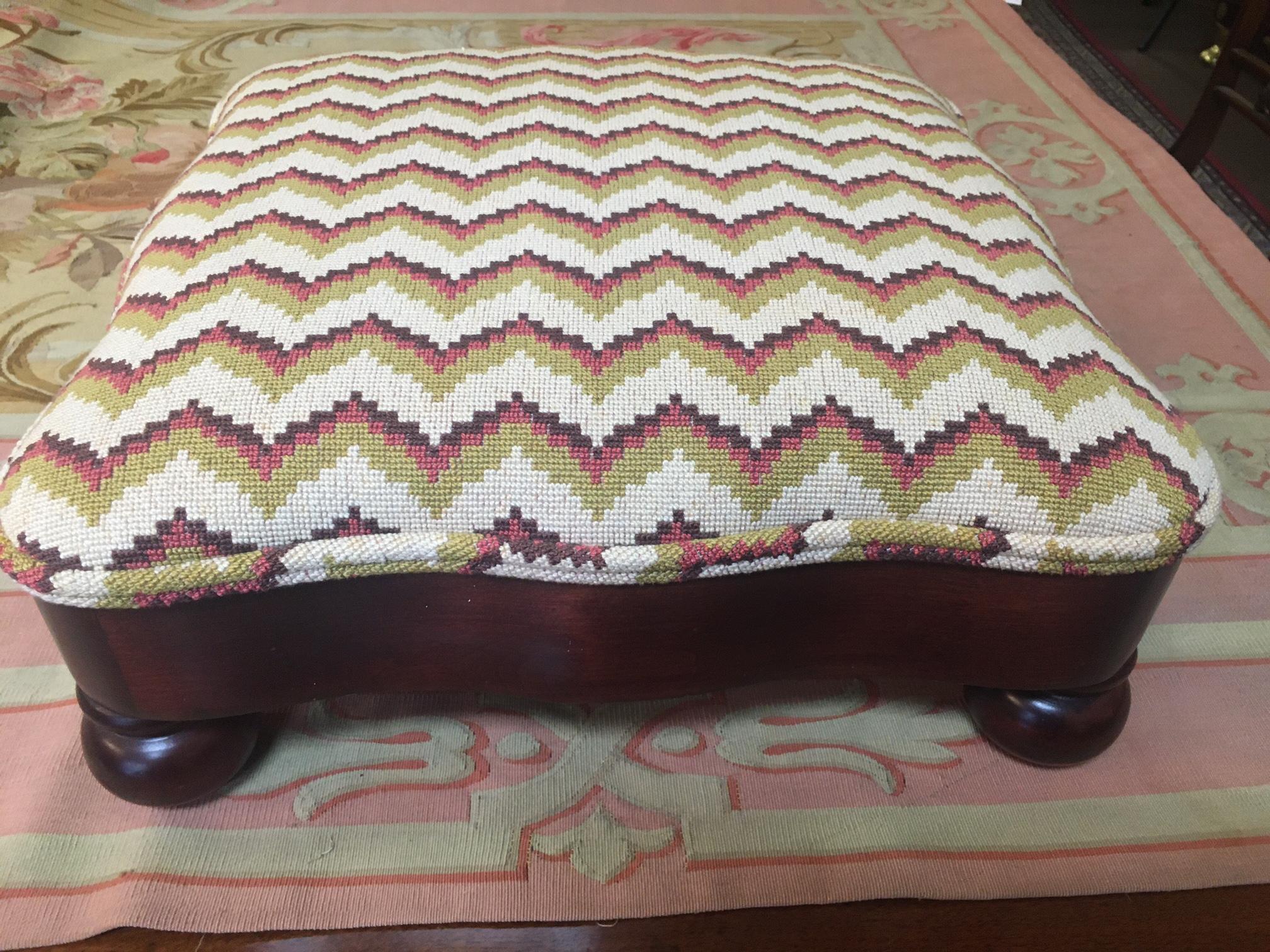 Ce grand tabouret carré en acajou présente des côtés serpentins, des pieds ronds en forme de chignon et est tapissé d'un attrayant motif à l'aiguille en chevron dans des couleurs crème, or et rouille. Une belle pièce qui peut être utilisée presque