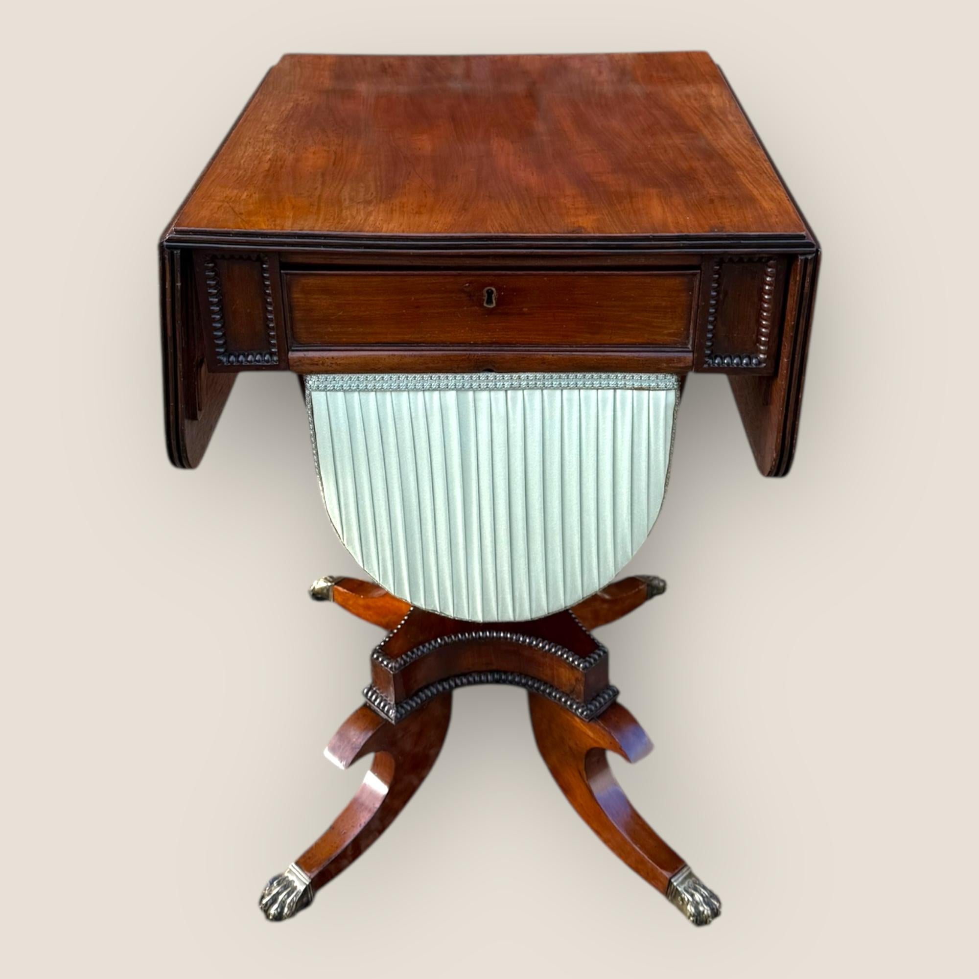 Here we have a Regency (1811-1830) mahogany sewing table. Featuring two drawers to the frieze, one either side and a fabric lined basket, which also slides open. The base, with gadrooned edges, has 4 shaped splayed legs each with brass lion claw