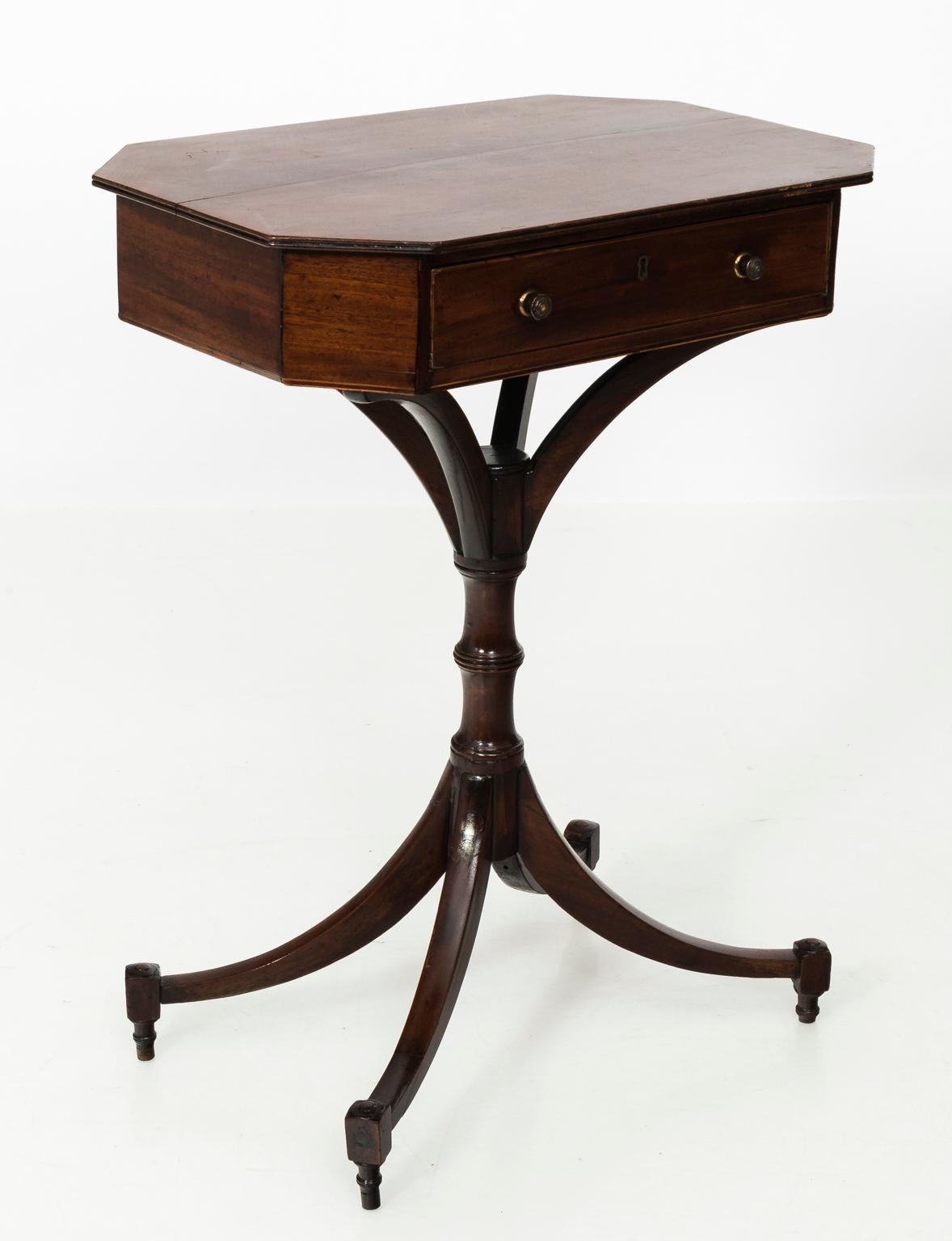 1820s Regency style mahogany side table with an octagonal tabletop, two drawers, and brass hardware. The body also features a faux bamboo pedestal, and four sabre legs.
 