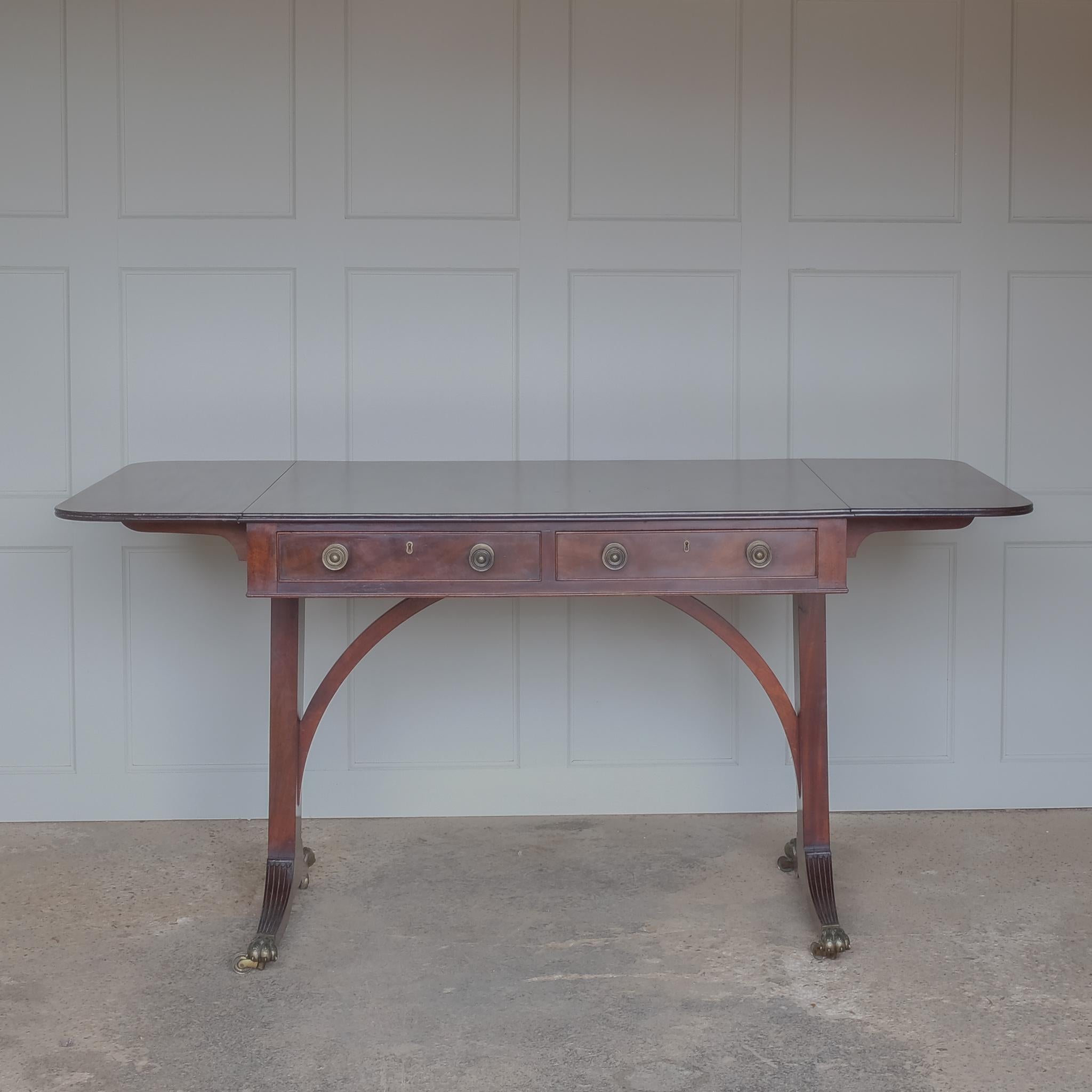An elegant Regency mahogany sofa table with two frieze drawers and matching faux drawers to the reverse, on tapered end supports with splayed and reeded feet with brass lion's paw caps and castors. The left drop leaf with some minor restorations. A