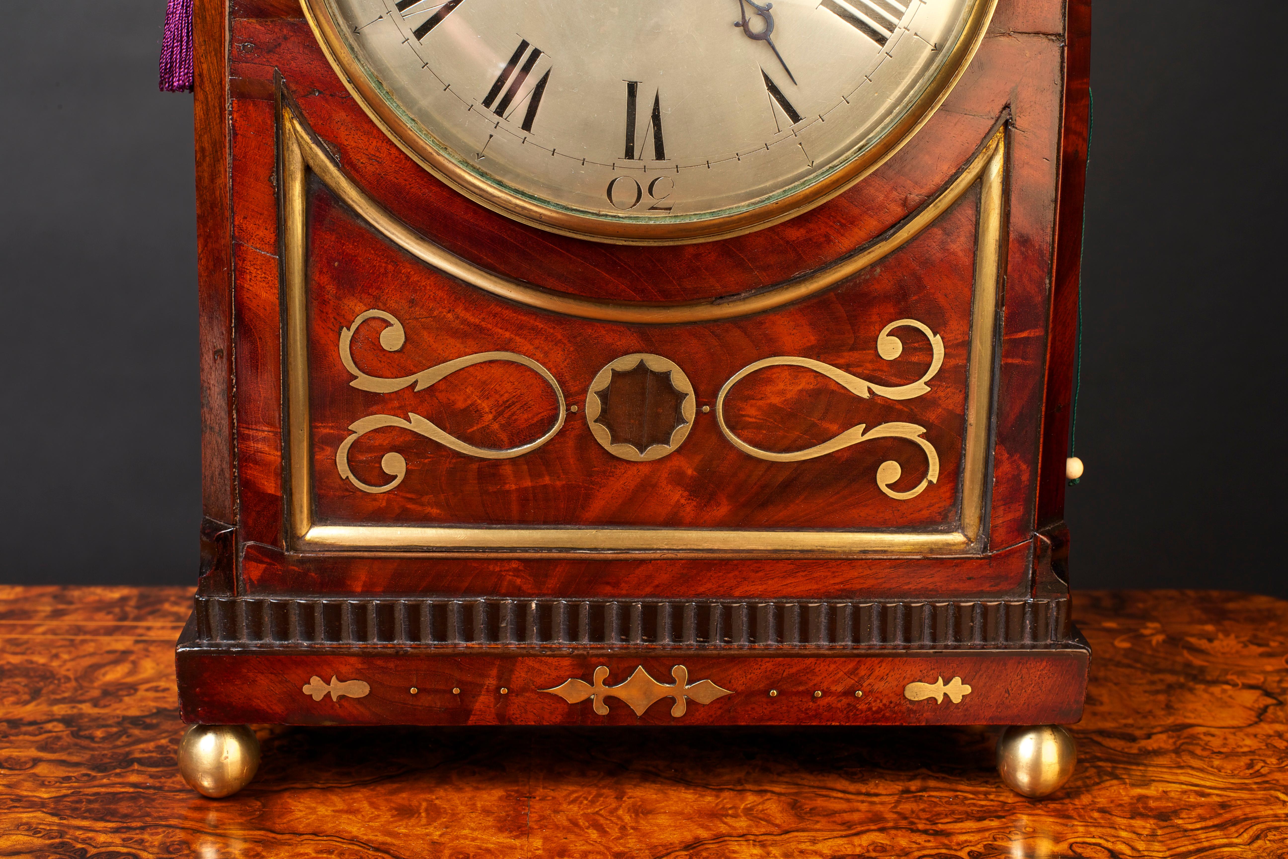 Regency mahogany bracket clock by Joseph Cross. Flame mahogany break arch top bracket clock with canted corners and brass fishscale sound frets and surmounted by a brass carrying handle. The clock standing on a raised plinth with silvered convex