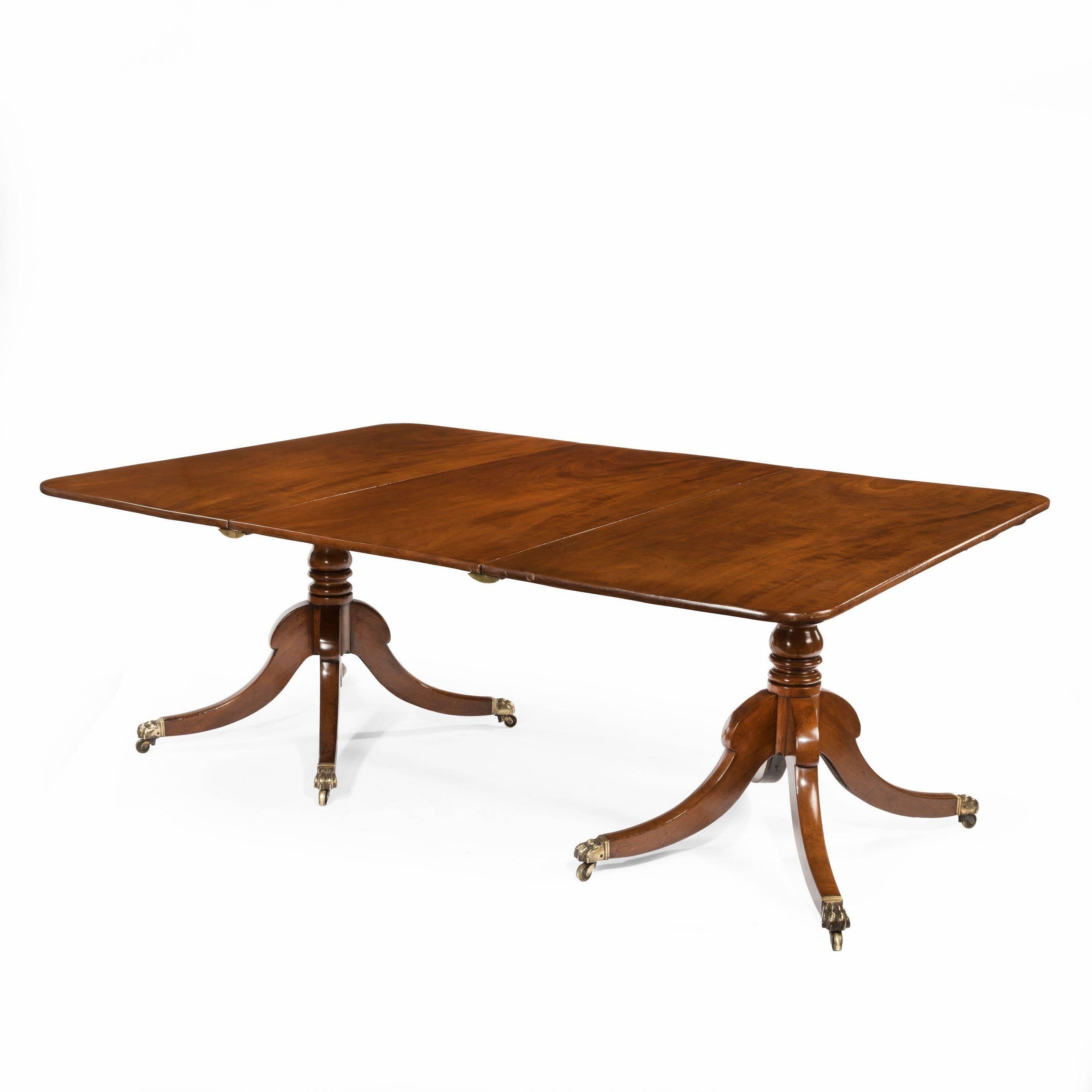 A Regency mahogany twin pillar dining table, of rectangular form with two shaped ends and an additional original leaf, raised on two central turned pillars, each with four high shouldered splayed legs terminating in brass lion’s paw castors,