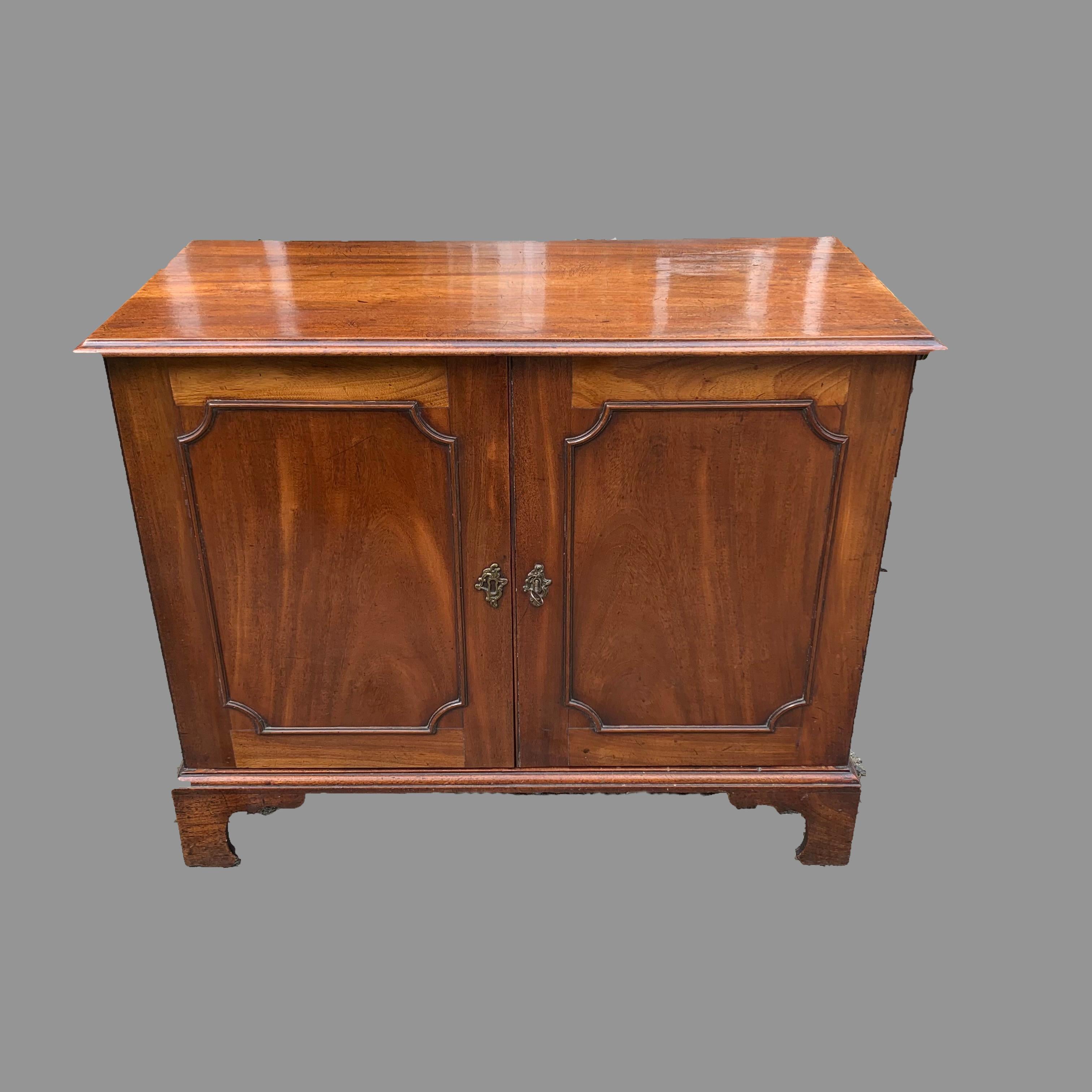 An unusual early 19th century mahogany two door side cabinet. The moulded edge top above a pair of panelled doors with moulded concave-cornered surrounds, enclosing the interior with one sliding tray, space for a second sliding tray and two
