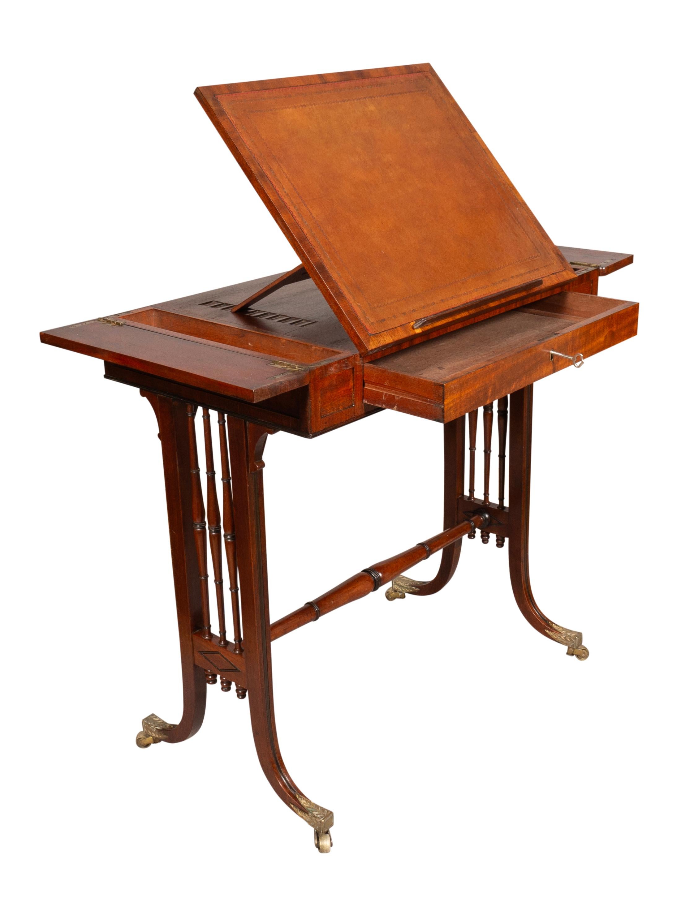 With a rectangular top with leather writing surface that can adjust. The ends with hinged compartments. The frieze with a drawer. Raised on a trestle base with spindles and turned stretcher ending on curved legs with brass cup casters with pointed