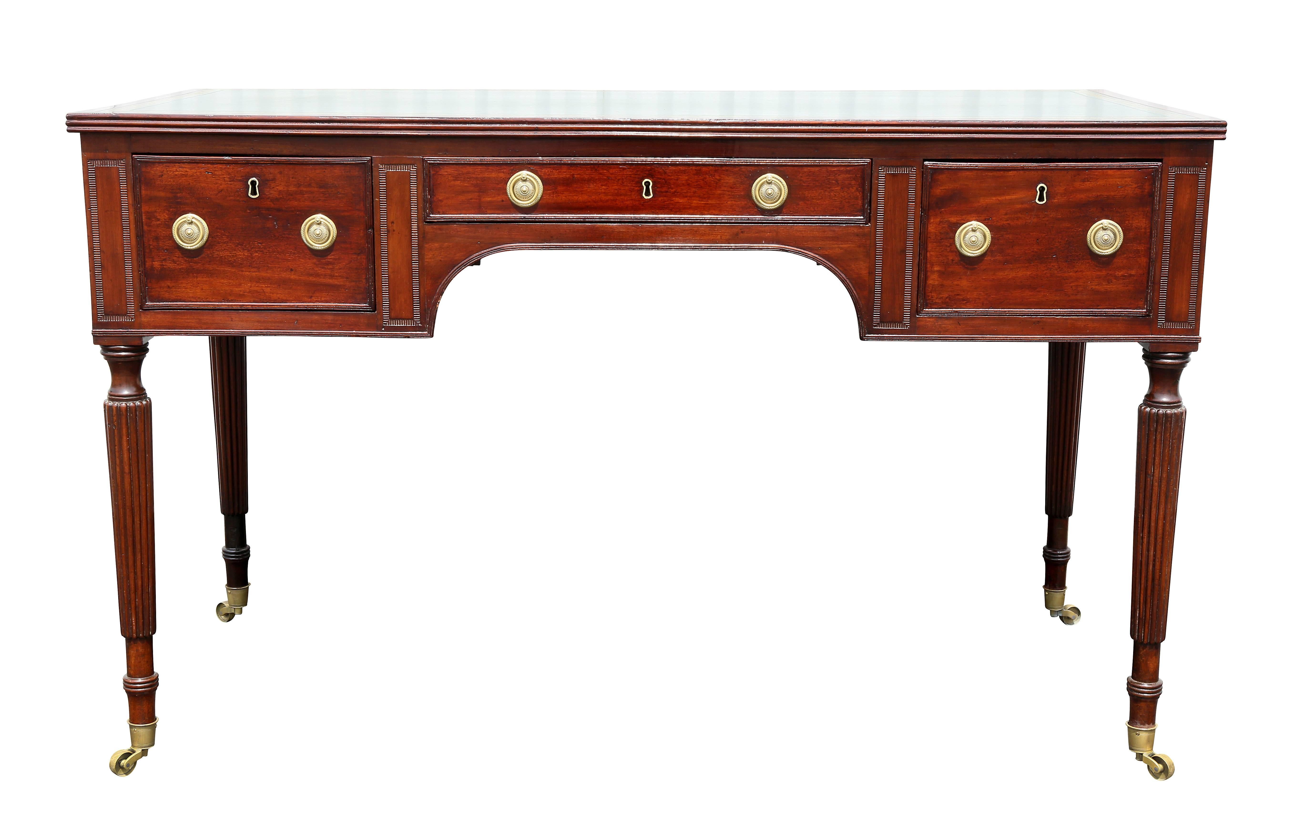 With rectangular top with inset green leather over a central drawer flanked by a pair of drawers with opposing false drawers raised on circular tapered reeded legs ending on casters.