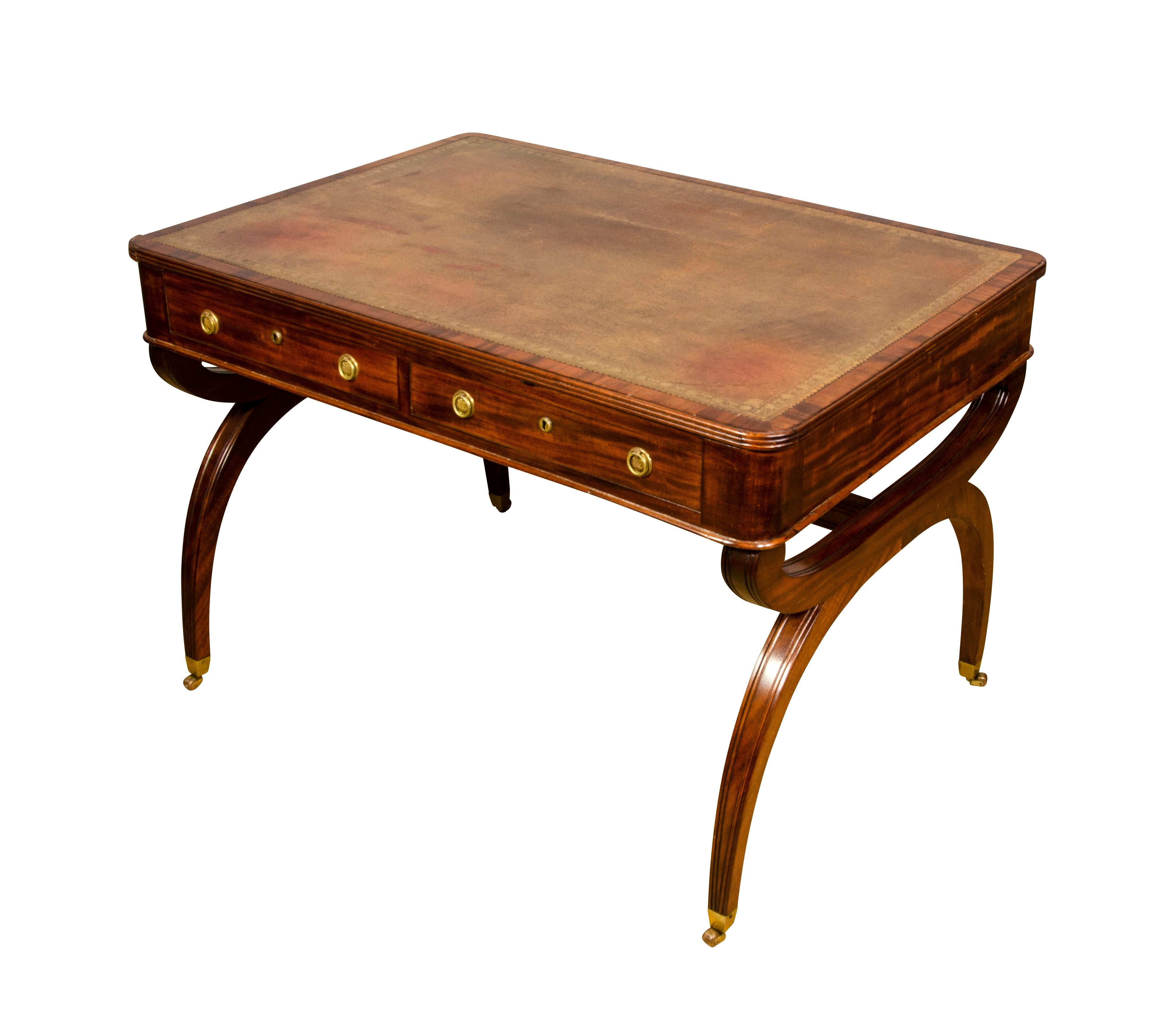 With rectangular top with inset brown leather over a frieze containing two drawers and opposing drawers all with brass ring handles raised on saber legs and casters.