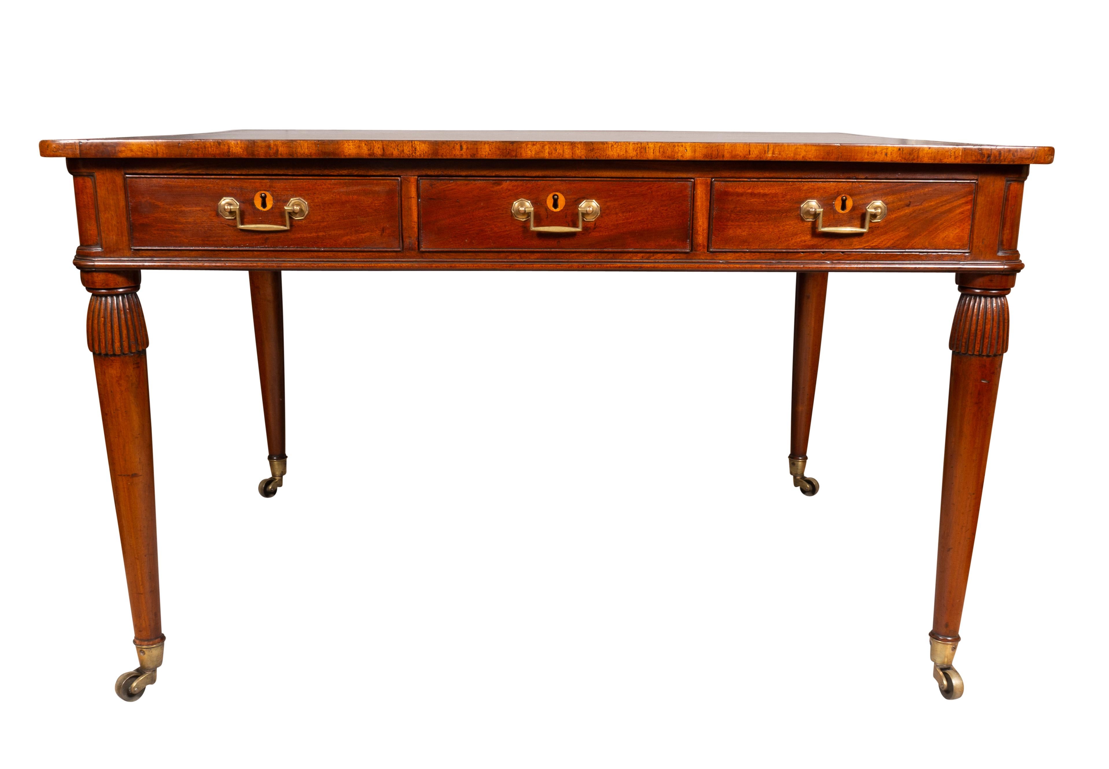 With a rectangular brown tooled leather top and banded border over three drawers with square bail handles and opposing working drawers so can work as a partners desk. Raised on circular tapered legs headed by reeded tassel carving.Raised on brass