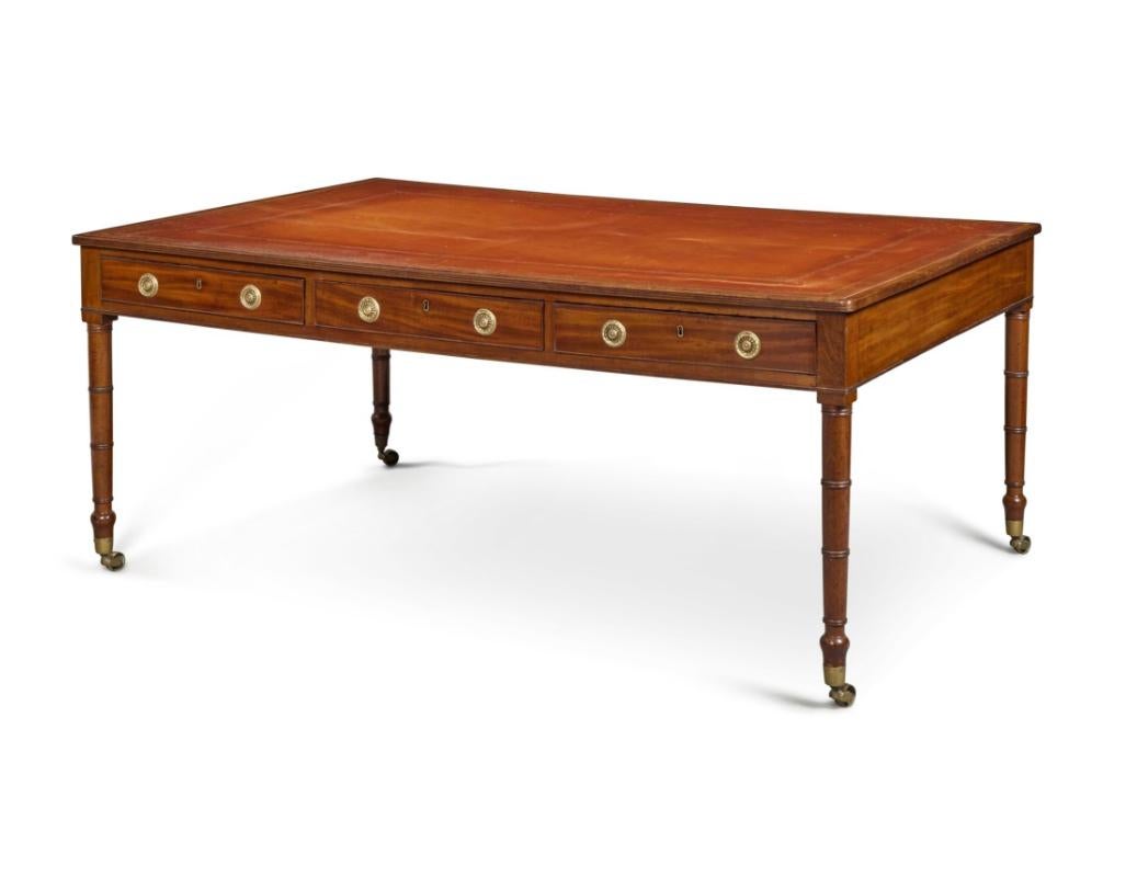 Rectangular top with inset tooled red leather top and cross banded edge over three drawers front and back. Raised on circular tapered legs. Casters. Sold Bonhams , London, February 12th 2002. Lot 71 and Hyde Park Antiques NYC.