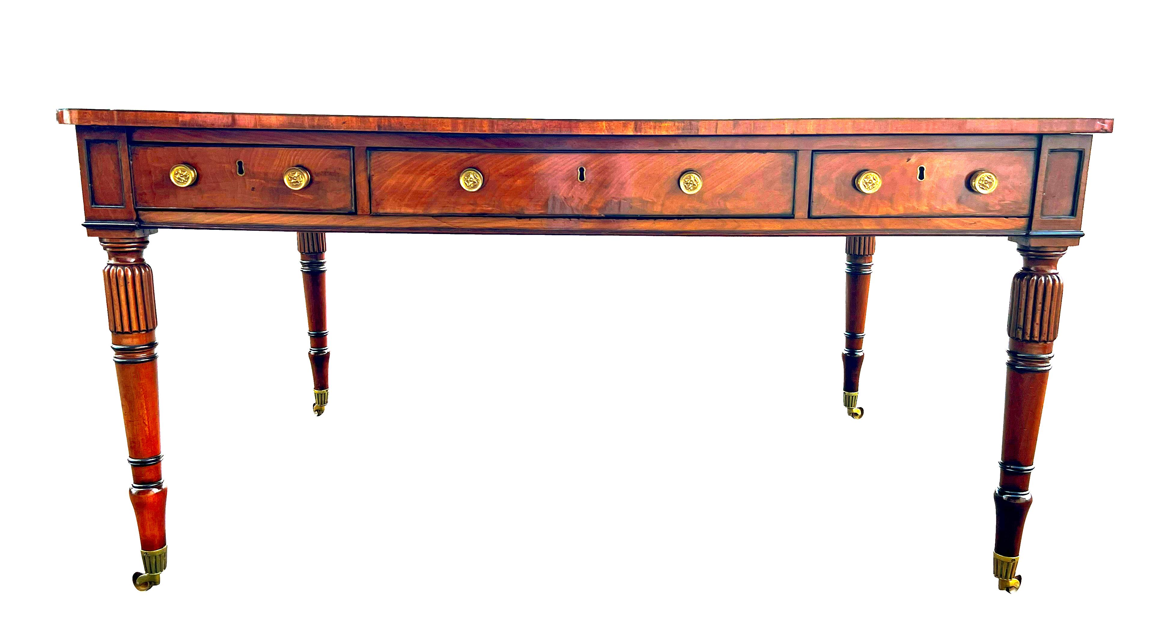 With inset tooled brown leather top with cross banded edge over a frieze containing three drawers and on the reverse three working drawers. False drawers on ends. All with brass knobs. Raised on turned tapered legs headed by  reeding. Ending on cup