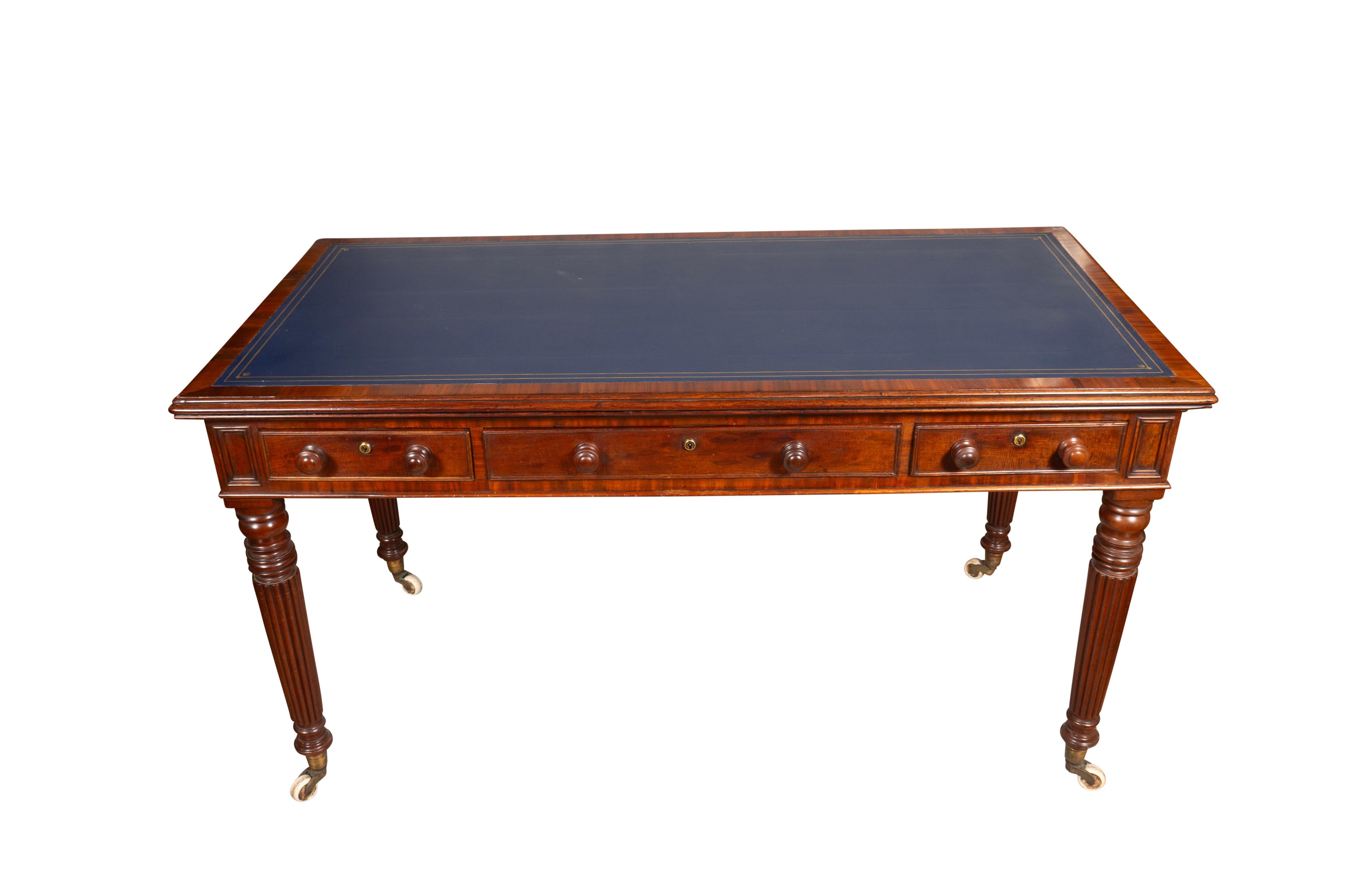 With a rectangular top with a new inset tooled blue leather with cross banded edge. The frieze containing a central long drawer flanked by a pair of drawers flanked by paneled ends.  Drawers with wood knobs. Back finished. Raised on turned tapered
