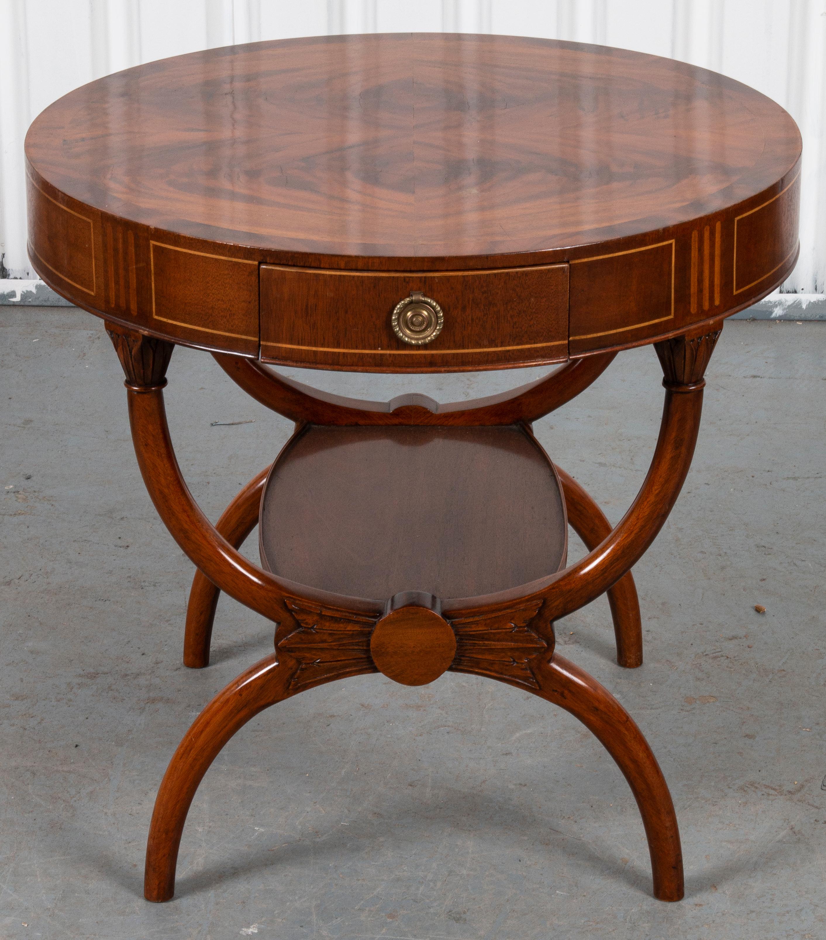 Regency round occasional table, the round top with inlaid details and a carved Curule form tiered base. 

Dimensions: 26” H x 27.5” D.