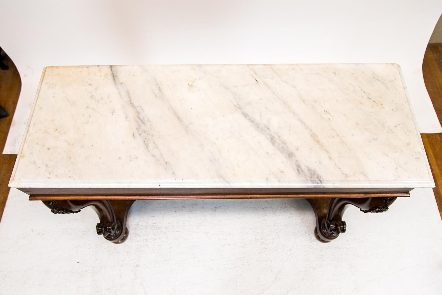 This Regency marble top console table has a Bianca Carrara marble top with an ogee edge. The shaped front legs have a carved floral motif and terminate in a volute scrolled foot that rests on a concave platform base.
  
