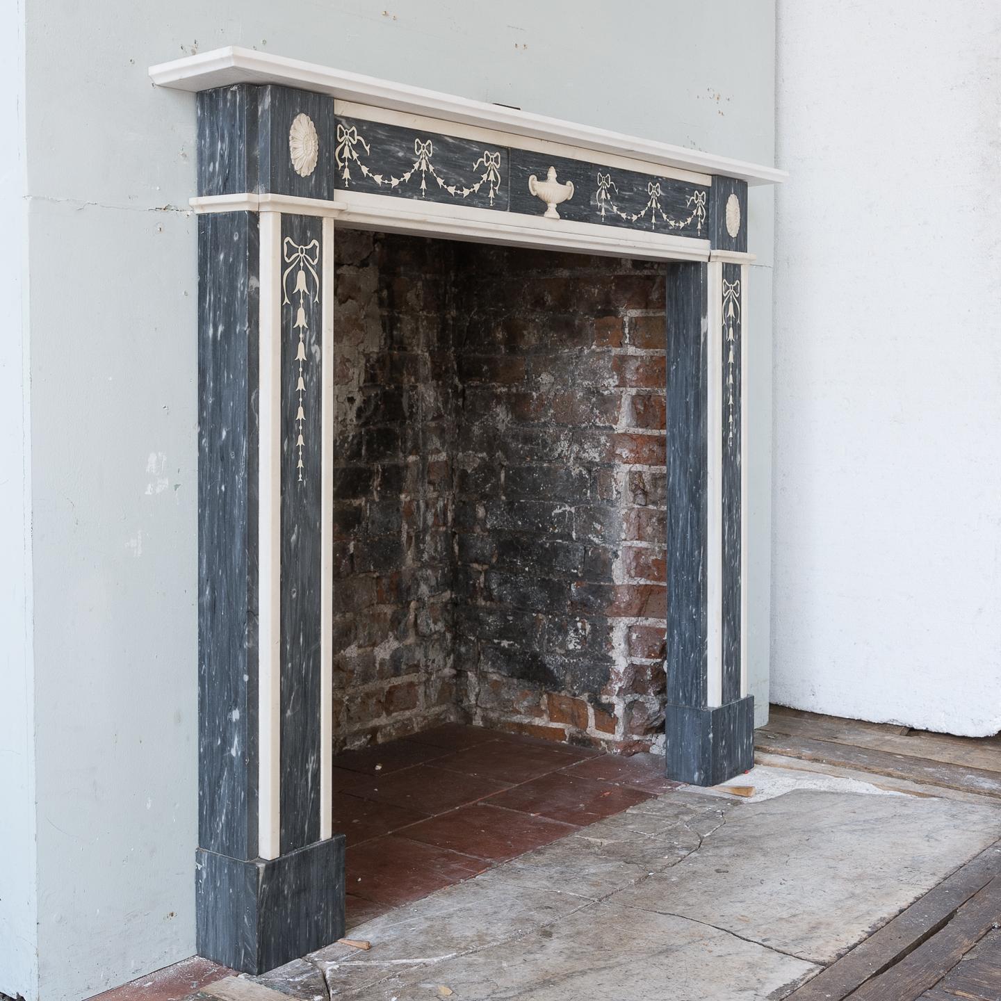Regency neoclassical inlaid dove grey and statuary marble fireplace, the moulded shelf above frieze with delicate scagliola inlay of swags and tied ribbons, centered by plaque with carved urn, the corner-blocks with carved paterae above jambs with