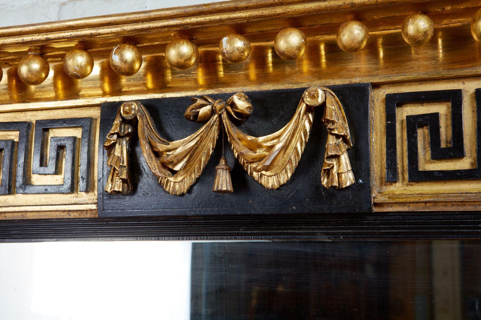 Fine early 19th century English gilt and ebonized wood triple plate overmantel mirror, the stepped pediment with brightly burnished gilt balls, the center tablet having swagged drapes surmounted by ebonized Greek key applied ornament flanked by