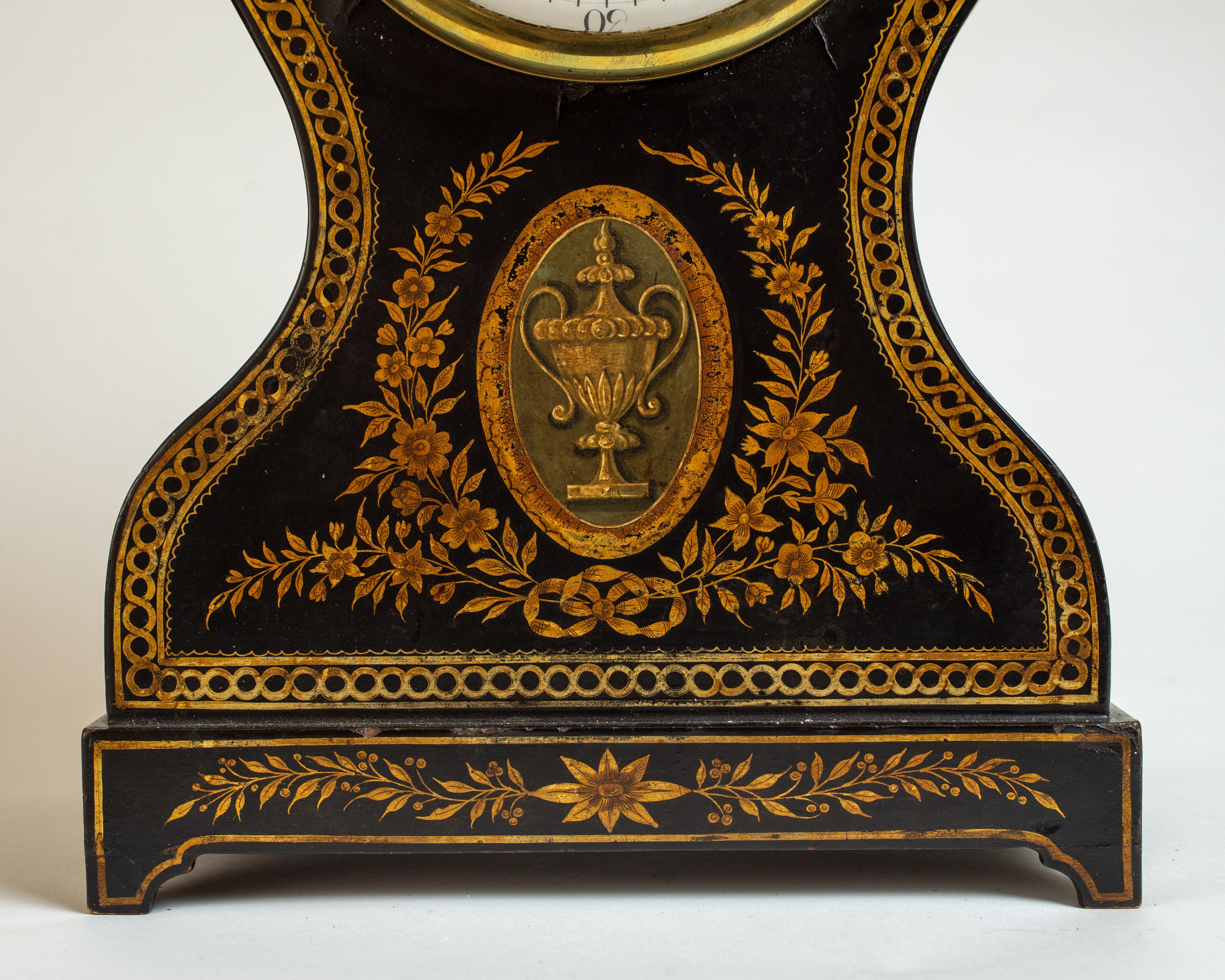 The waisted sides surmounted by a brass urn finial, above a rectangular base raised on bracket feet, decorated with braided border and depictions of floral swags, garland, and hunt trophies, the porcelain dial with Roman numerals and Arabic numerals