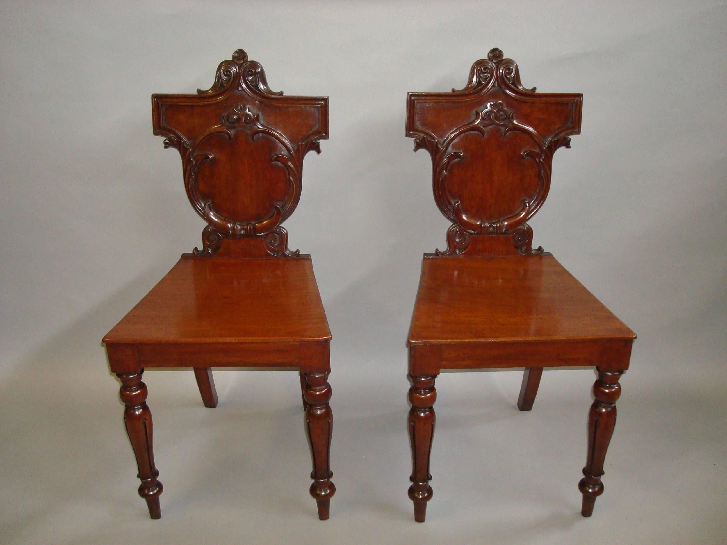 Late Regency pair of Irish mahogany hall chairs; the very shapely shield backs with acanthus scroll carving and moulded surround, headed with acanthus and flower head decoration with an interesting celtic motif below, the figured mahogany seats of