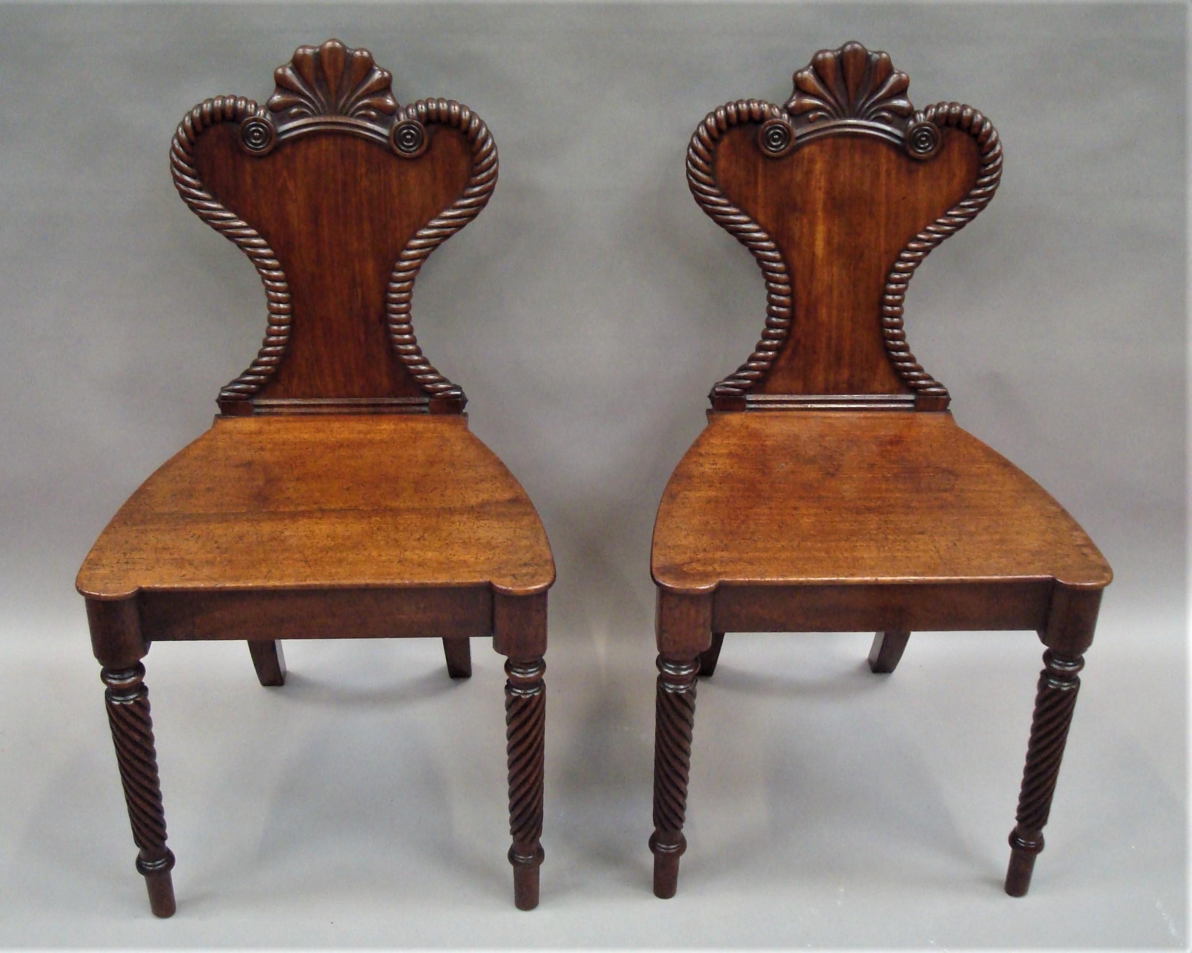 Good Regency pair of mahogany hall chairs of unusual design; the waist shaped back headed with a carved anthemium with roundels below and a rope twist molded edge terminating with small carved roundels to the sides. The shaped seats with protruding