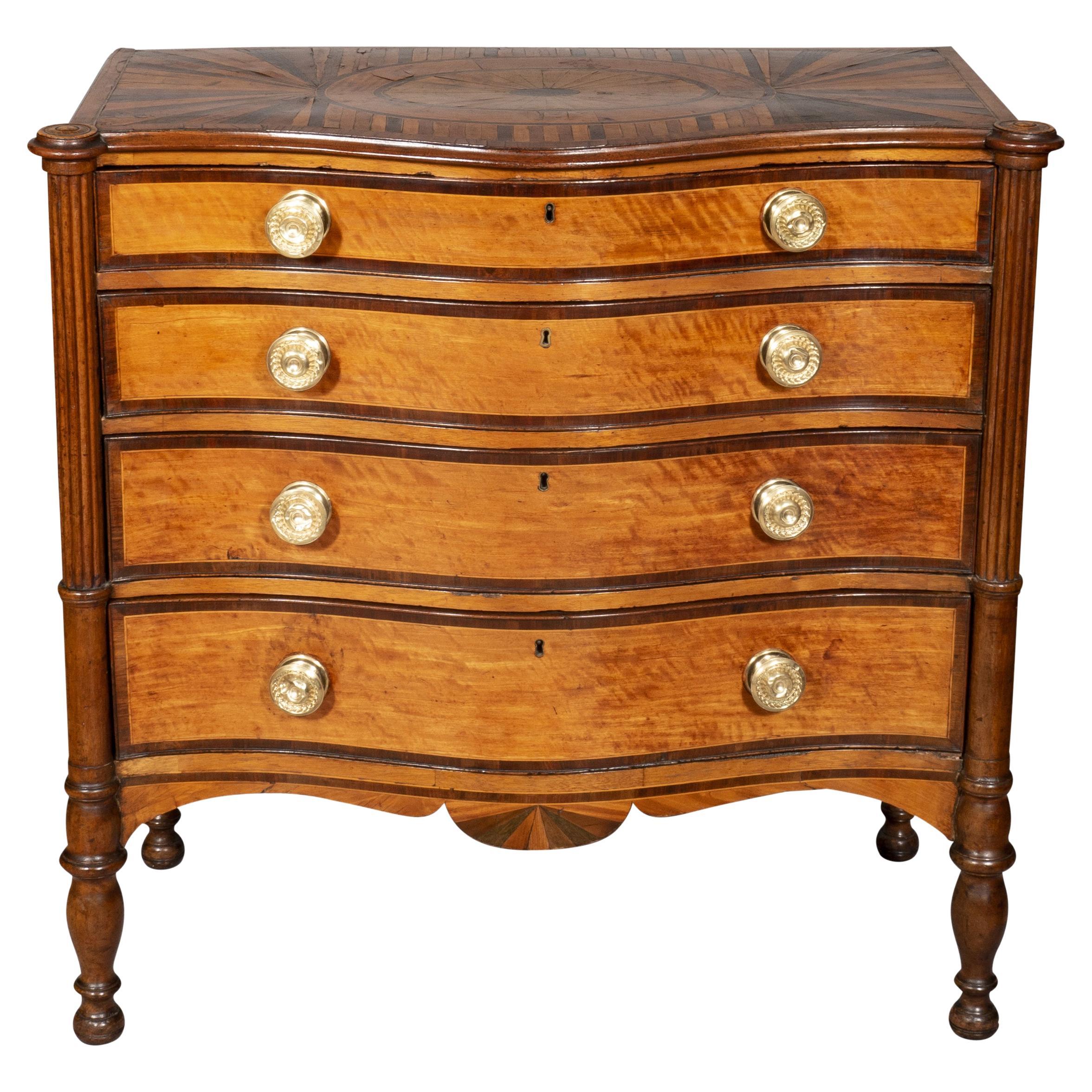 With a serpentine rectangular top with rounded cookie corners, elaborate sunburst inlays of exotic woods surrounding an oval paterae panel with punch work decoration. Over a fitted gentlemen's dressing drawer over three graduated drawers, all