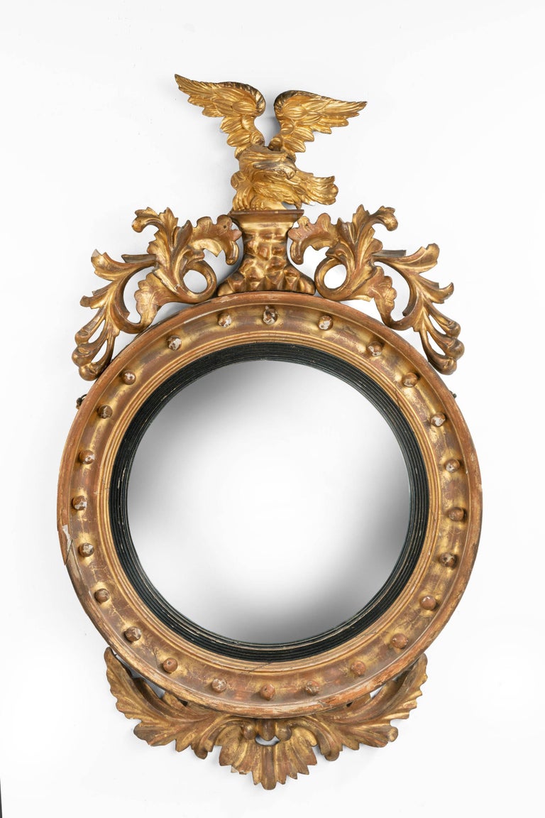 A Regency period, convex, circular mirror. Surmounted with a flying eagle. Scrollwork, foliage and eagle on a rocky base. Original gilding with less than two percent restoration.