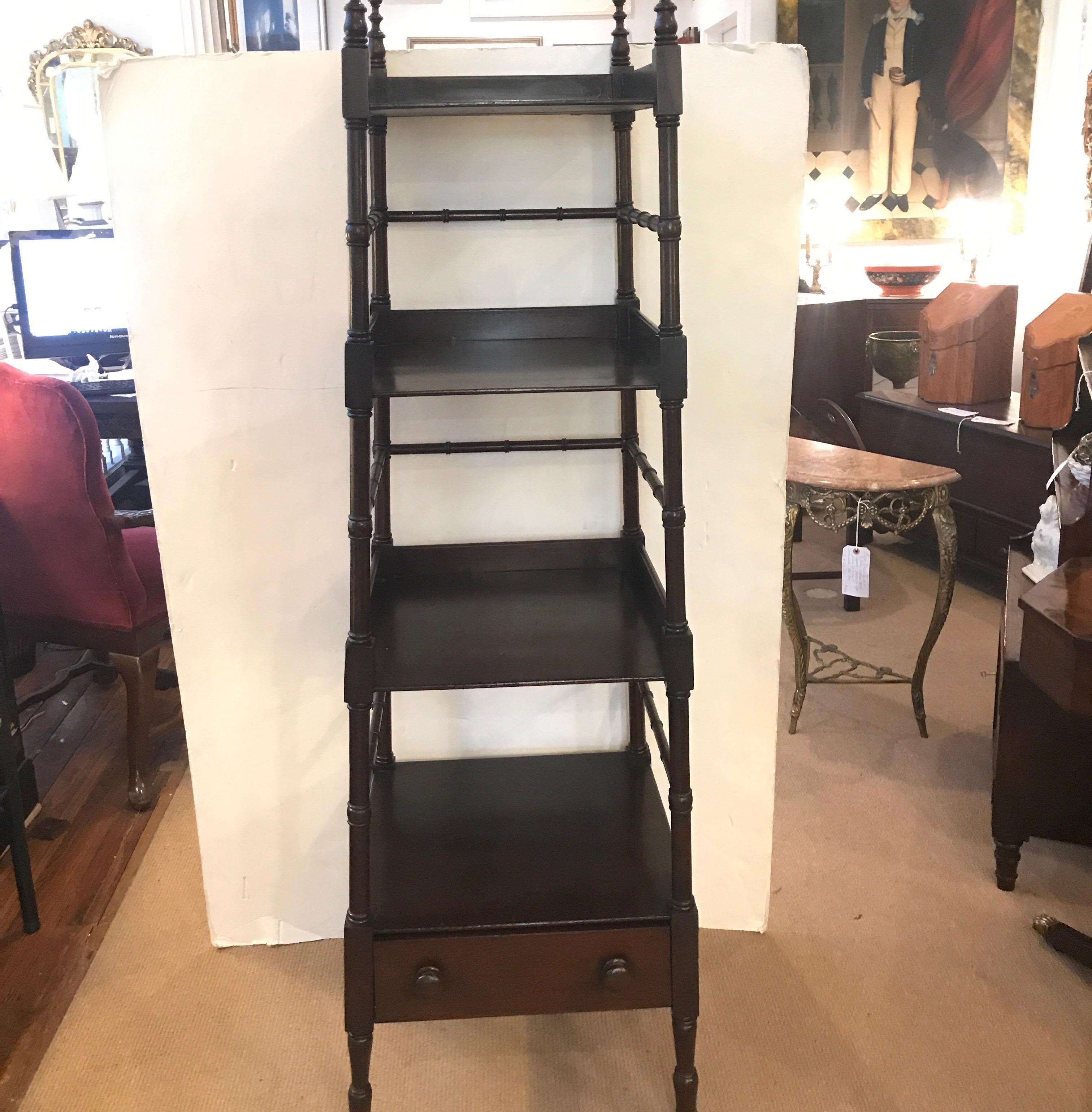 A mahogany four shelved what not shelf with lower drawer. The shelf unit with tapered form getting slightly larger from top to bottom. The top with four finials and the bottom with original brass castors.