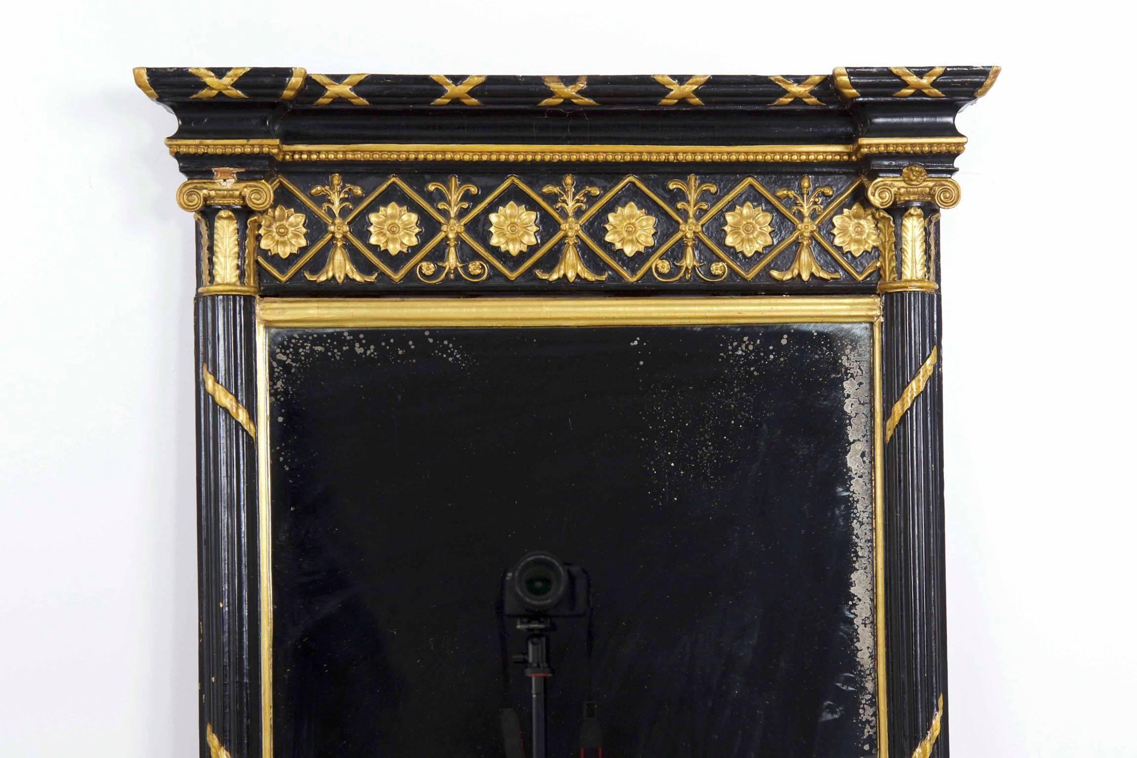 This elegant Regency period pier mirror is a practice in contrasts, utilizing a pure black pigment over gesso against the bright silvered glass and vibrant gilded highlights.  Borrowing from the French, the mirror incorporates a twisting and