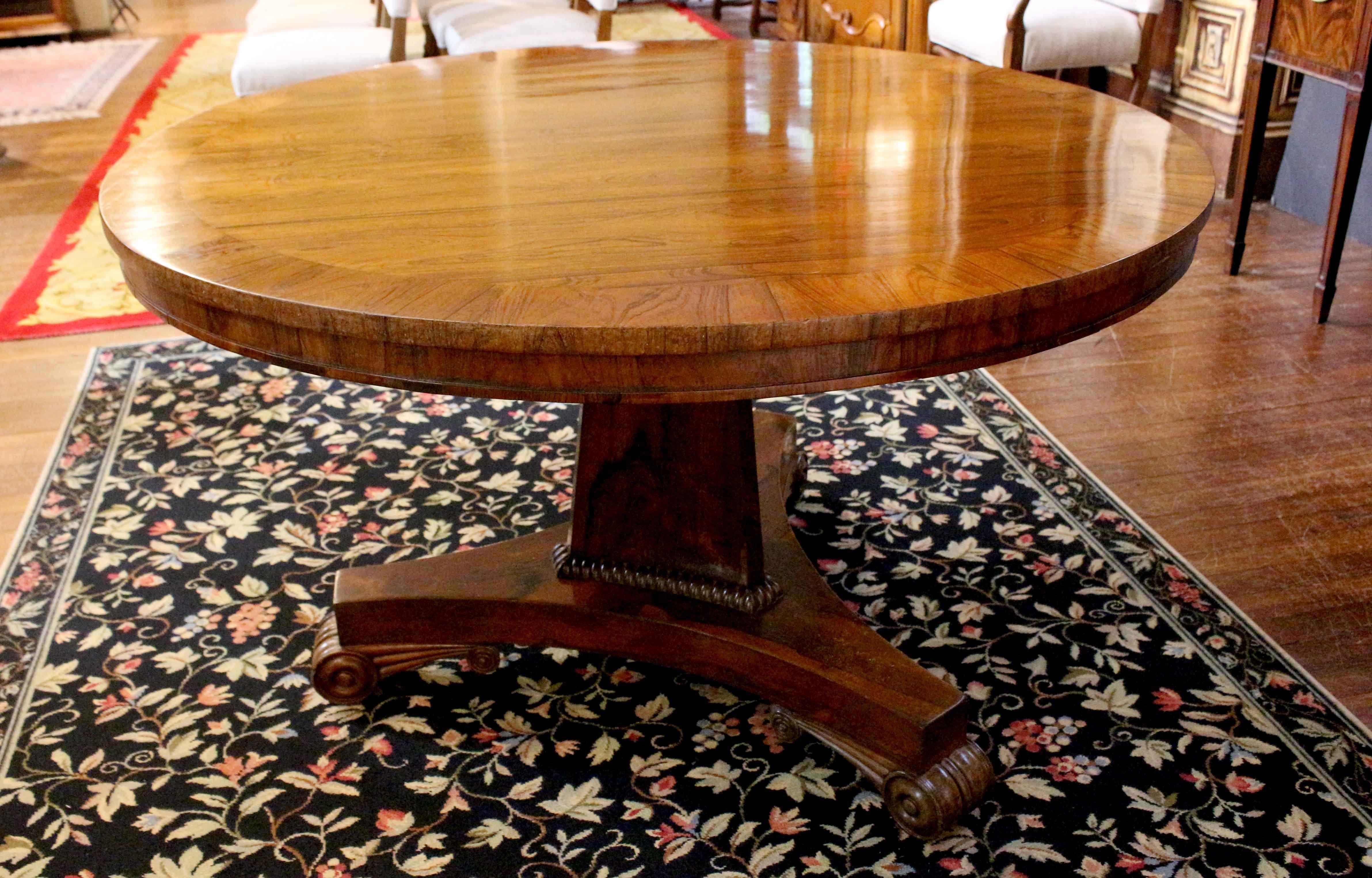 Regency period, early 19th century, center table, English. Rosewood with rosewood crossbanding. Raised on a faceted triangular pedestal with gadrooning and tripod base with pronounced scrolled, reeded & rosette carved feet on casters. Minor veneer