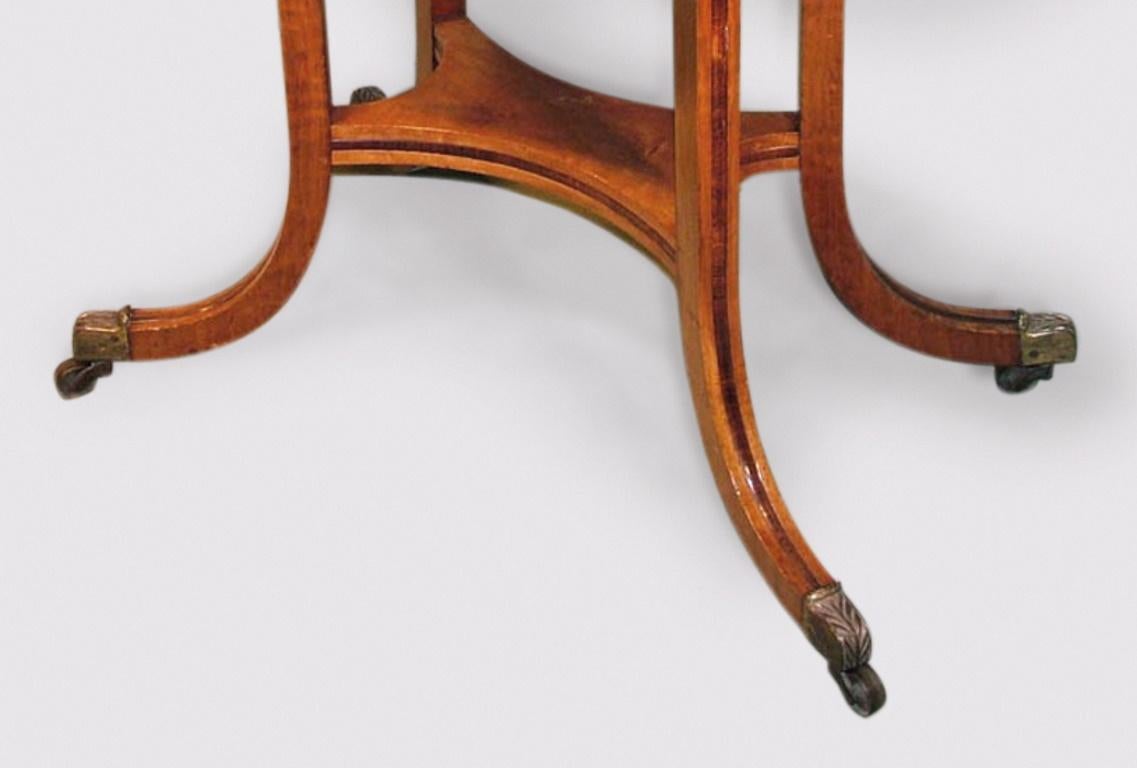An early 19th century Regency period well figured mahogany card table having rosewood crossbanded “D” shaped top above frieze supported on rosewood paneled “hockey stick” legs joined by similar concave rectangular shelf and ending on original