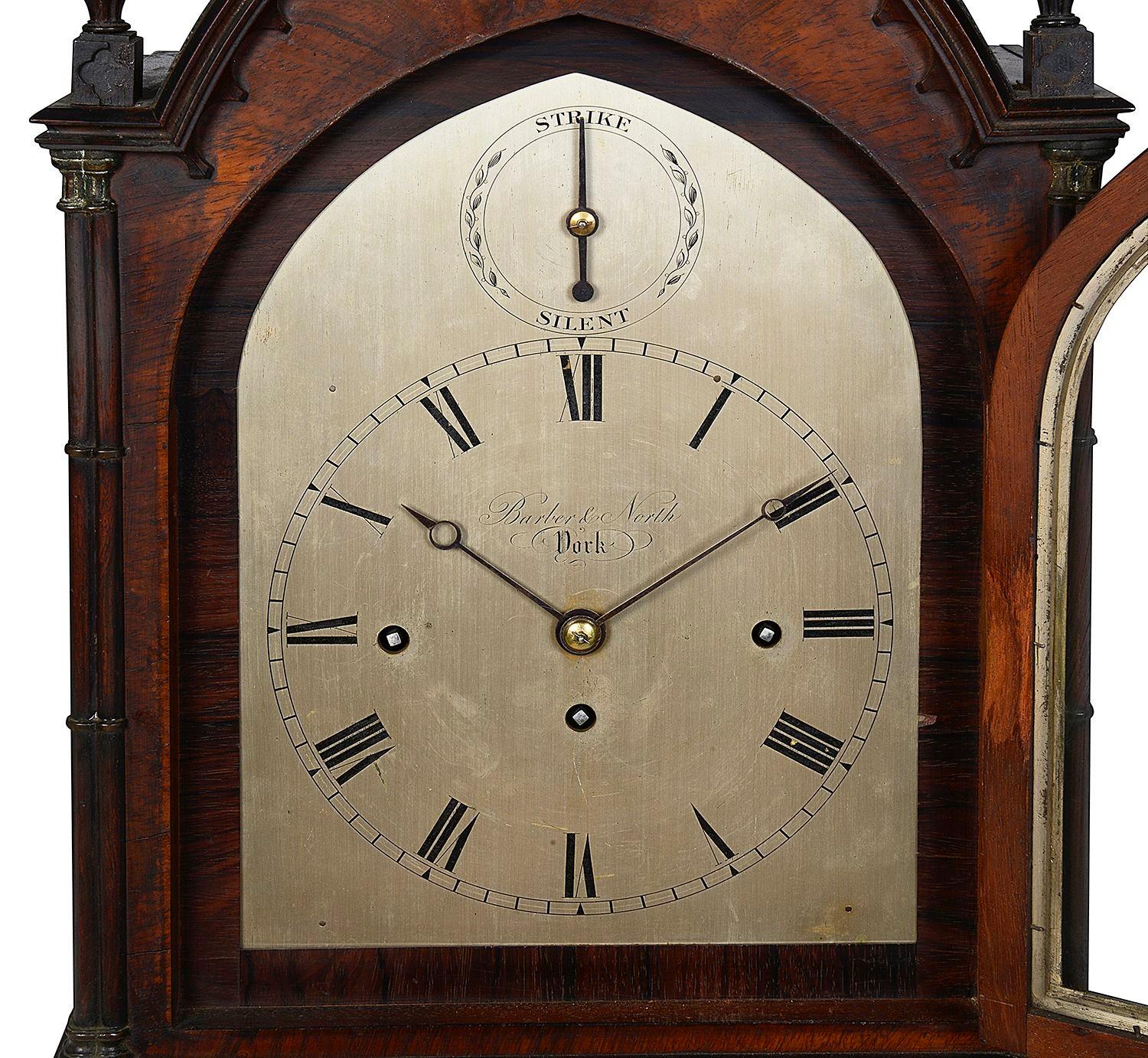 A very good quality Regency period Mahogany Gothic influenced mantel clock, having delicate carved finials, cluster columns to the sides, the silvered dial with Roman numerals, a three train movement, strike / silent feature, an eight day duration,