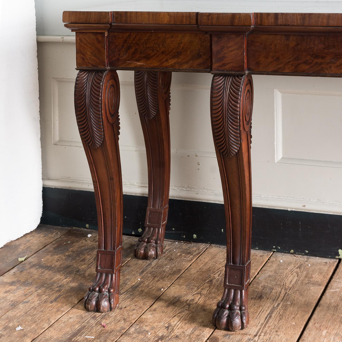 Early 19th century mahogany serving table, the breakfront top and frieze on six acanthus carved console legs terminating in lion’s paw feet.