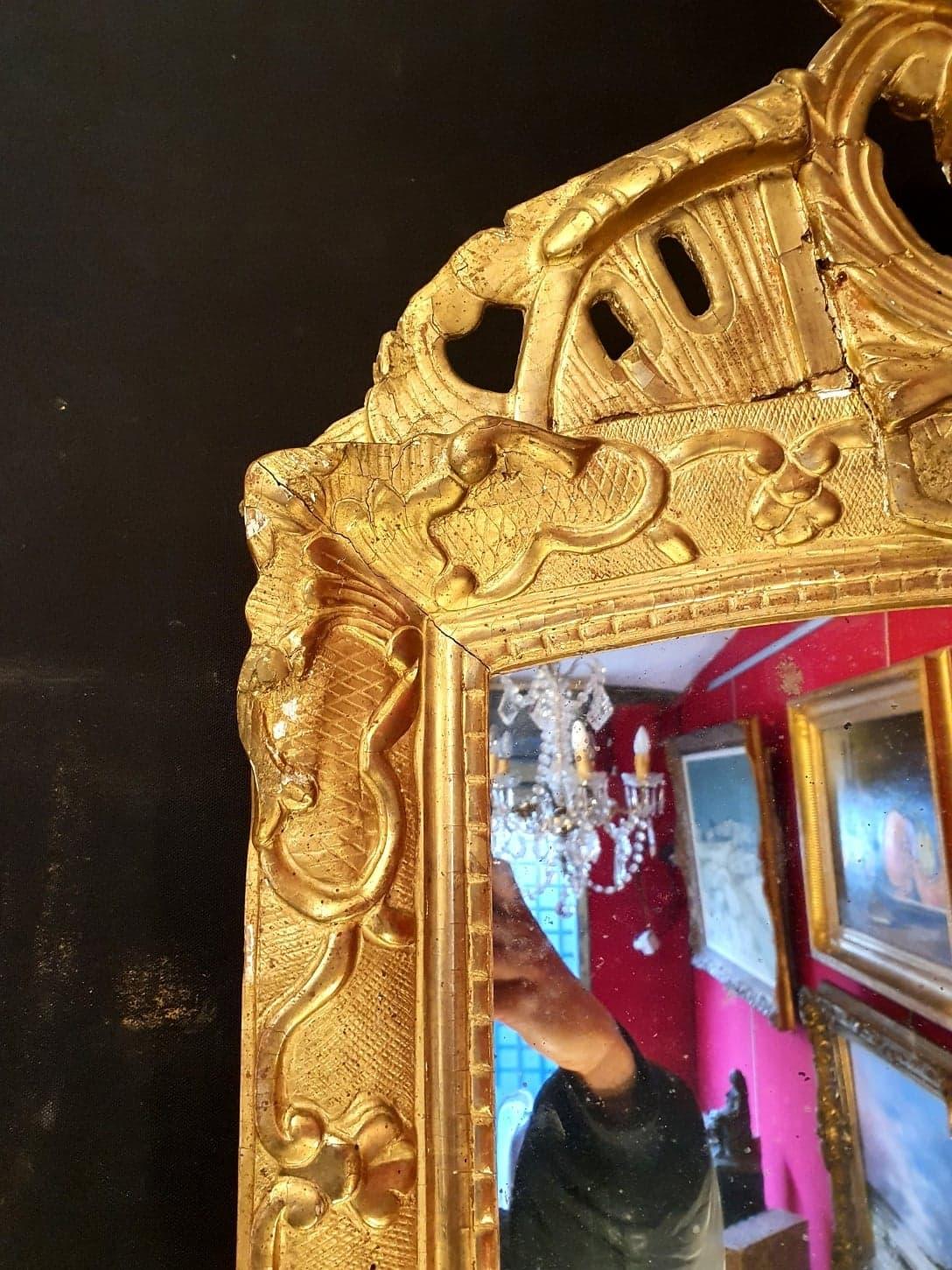 This pediment mirror is from the Regency period. It is entirely in carved and gilded wood. Also, this mirror has a pediment with floral decorations and is in good condition. In addition, the mirror is original and rests on its original parquet.