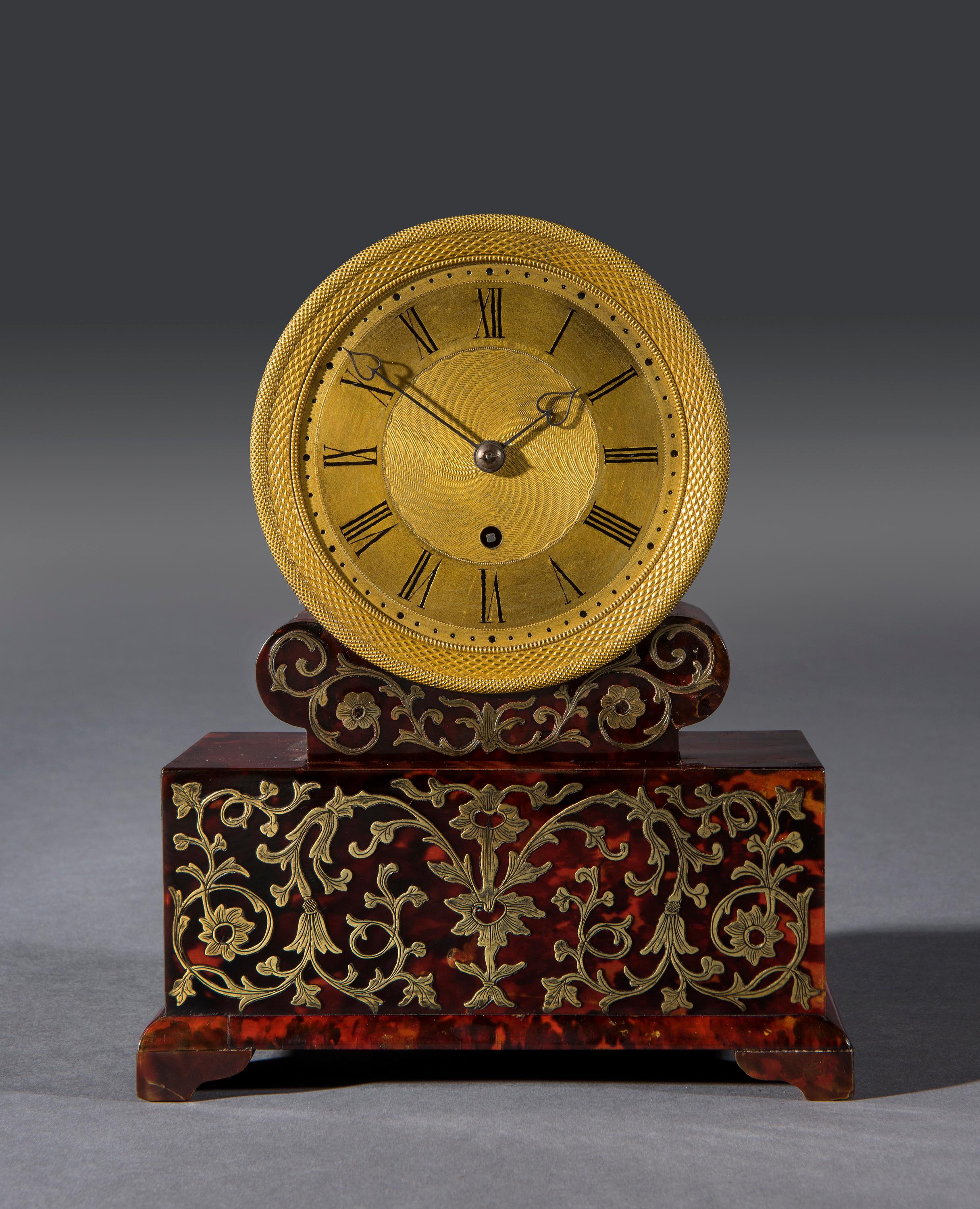 The marquetry inlaid boulle drumhead clock is veneered in red tortoiseshell with a finely gilt cast and etched dial with Roman numerals and heart-shaped arms. The back of the clock is veneered in rosewood and engraved with the clockmaker's name,