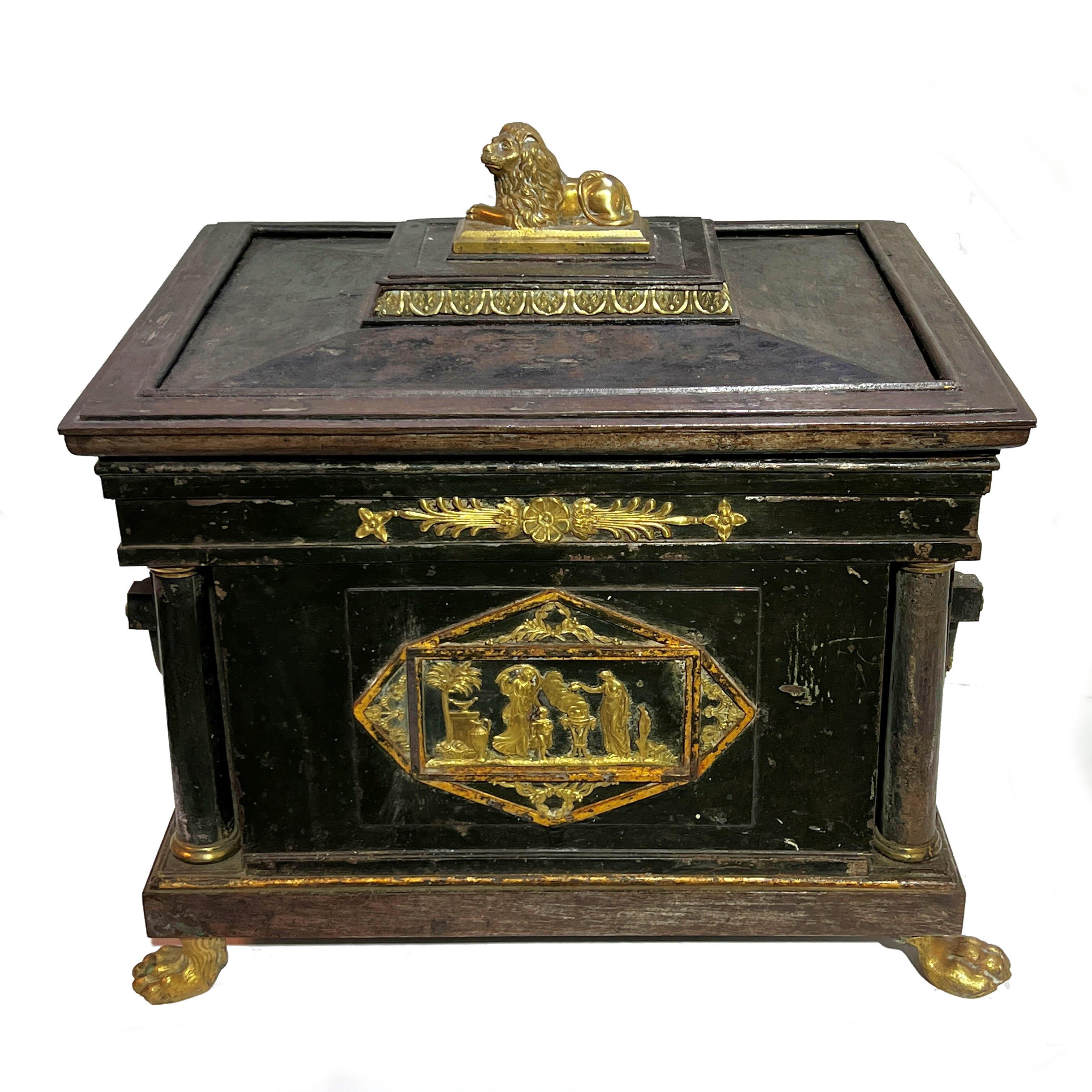 Our late Regency period strongbox features gilt neoclassical mounts including lion masks and rosettes at the sides, Roman Tuscan style columns at the front corners, figurative panel on front depicting Roman goddesses stoking a torchere, recumbent