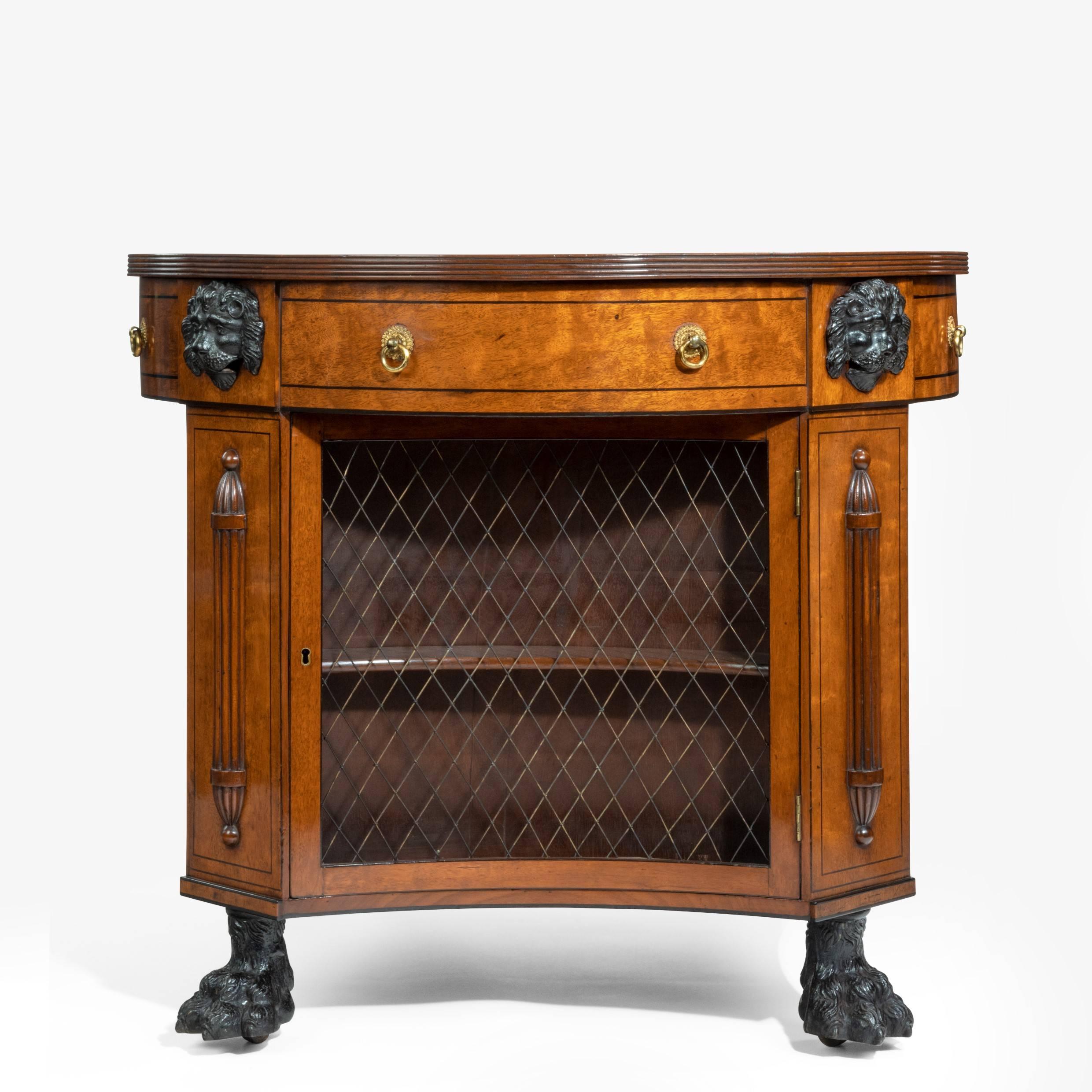 An unusual Regency plum-pudding mahogany library centre table and bookcase,
the circular top with four dummy frieze drawers with ring handles set above four shallow, concave bookcases enclosed behind the original trellis of brass wire, the uprights