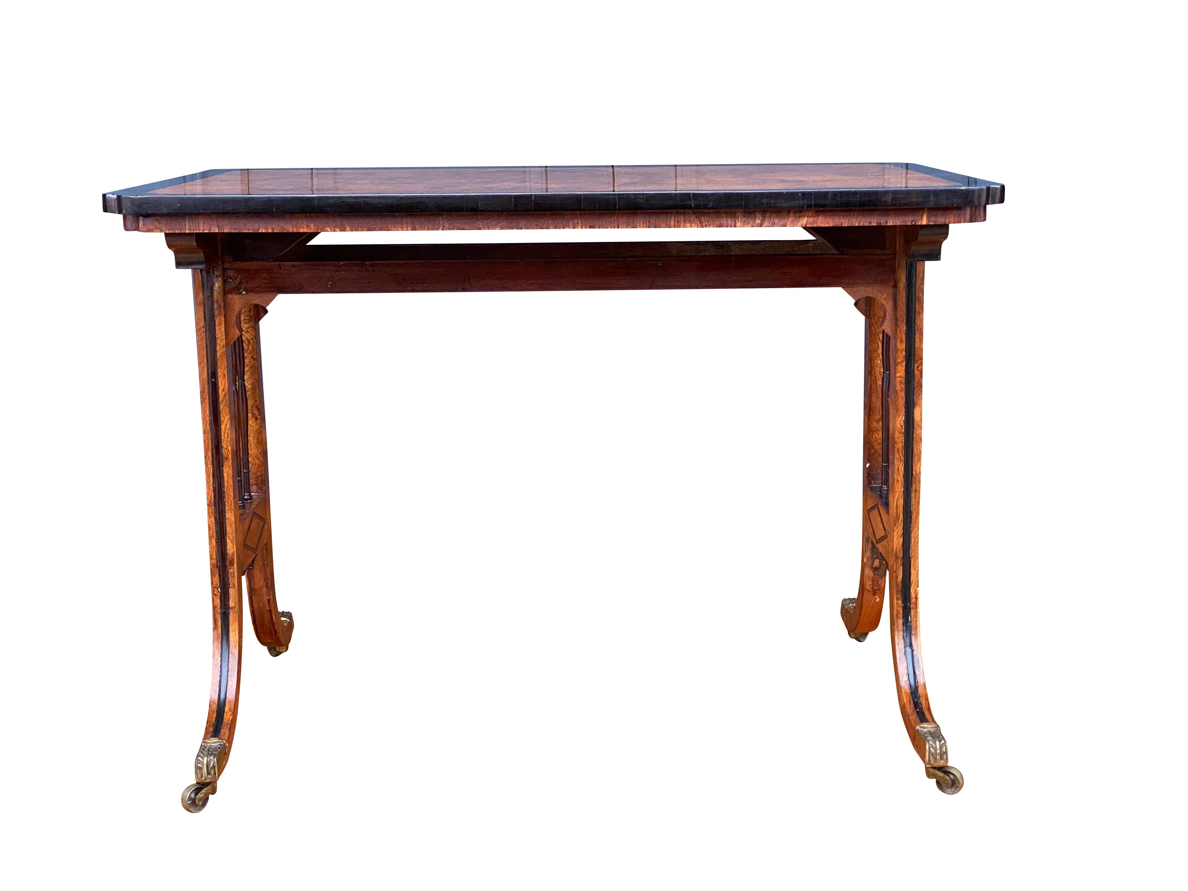 Figured wood top with crossbanded edge raised on trestle ends with spindles and diamond form applied molding, carved legs with brass casters. Almost identical example in 