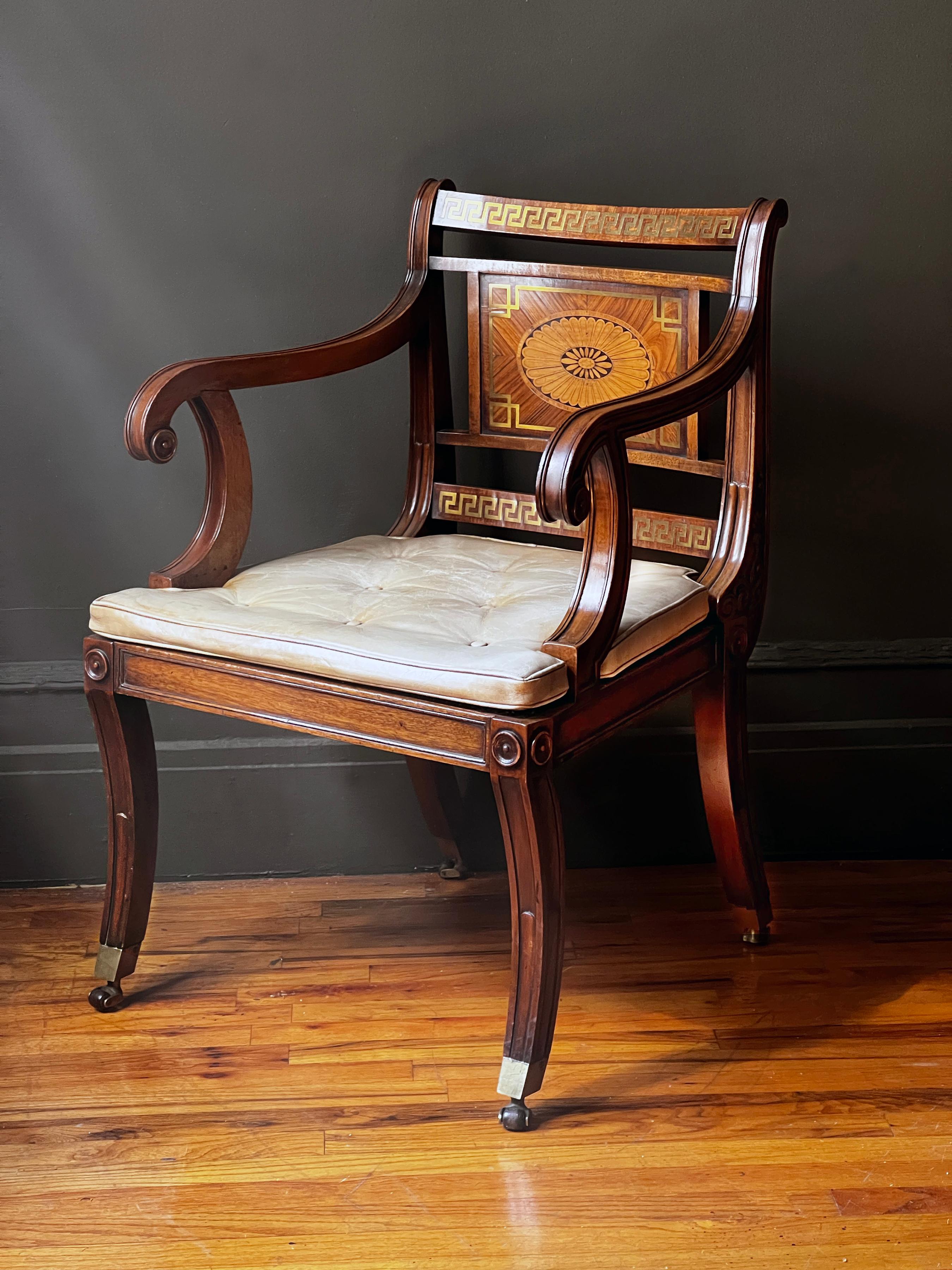 A handsome Regency style brass inlaid mahogany armchair with rosewood, satinwood and kingwood veneers, having paterae inlaid back panels over caned seat with leather upholstered squab cushions, standing on saber legs ending in box casters. England,