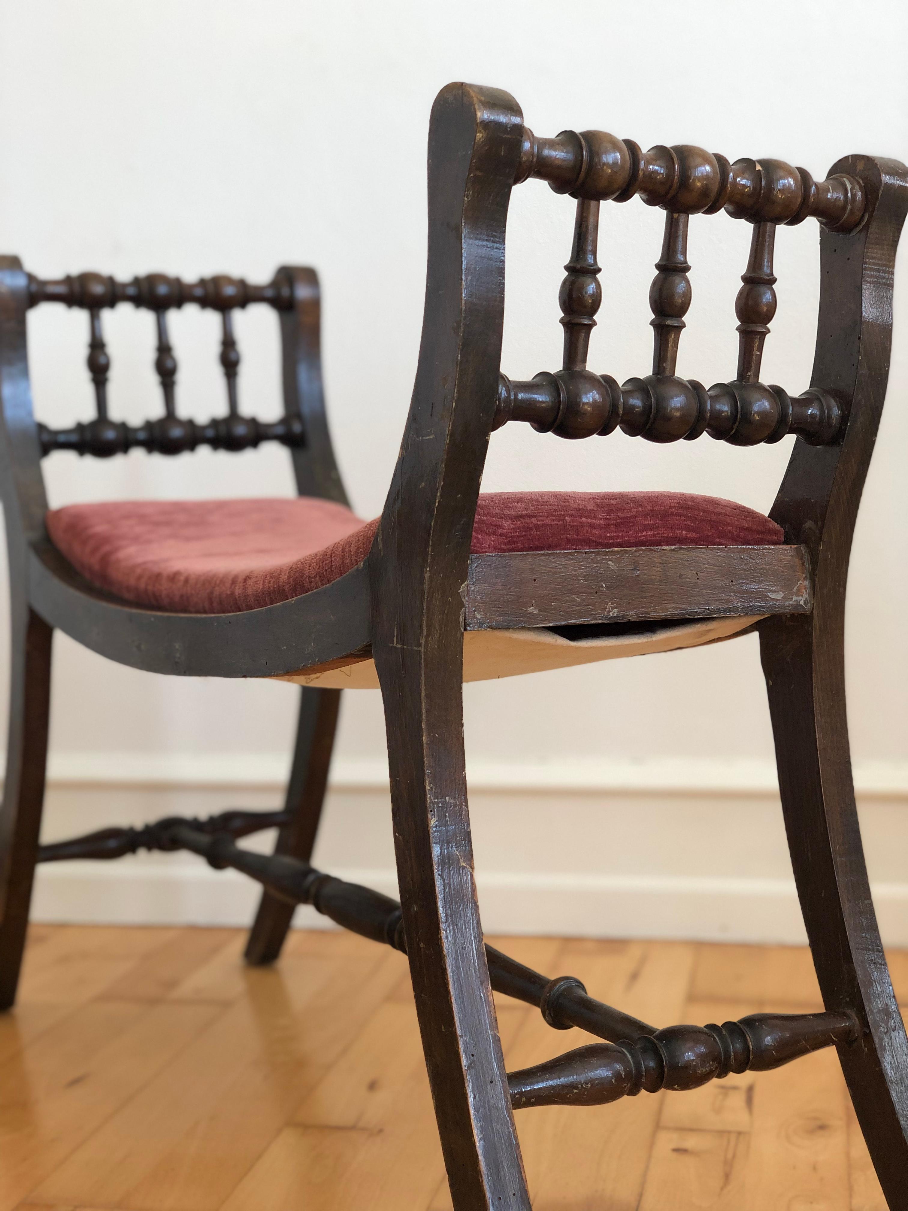 Antique wooden bench in Regency Revival style, dating from the early 20th century. Crafted from solid wood with turned spindle details on both ends and stretcher supports, finished in a dark stain. The seat is upholstered in a cranberry red textured