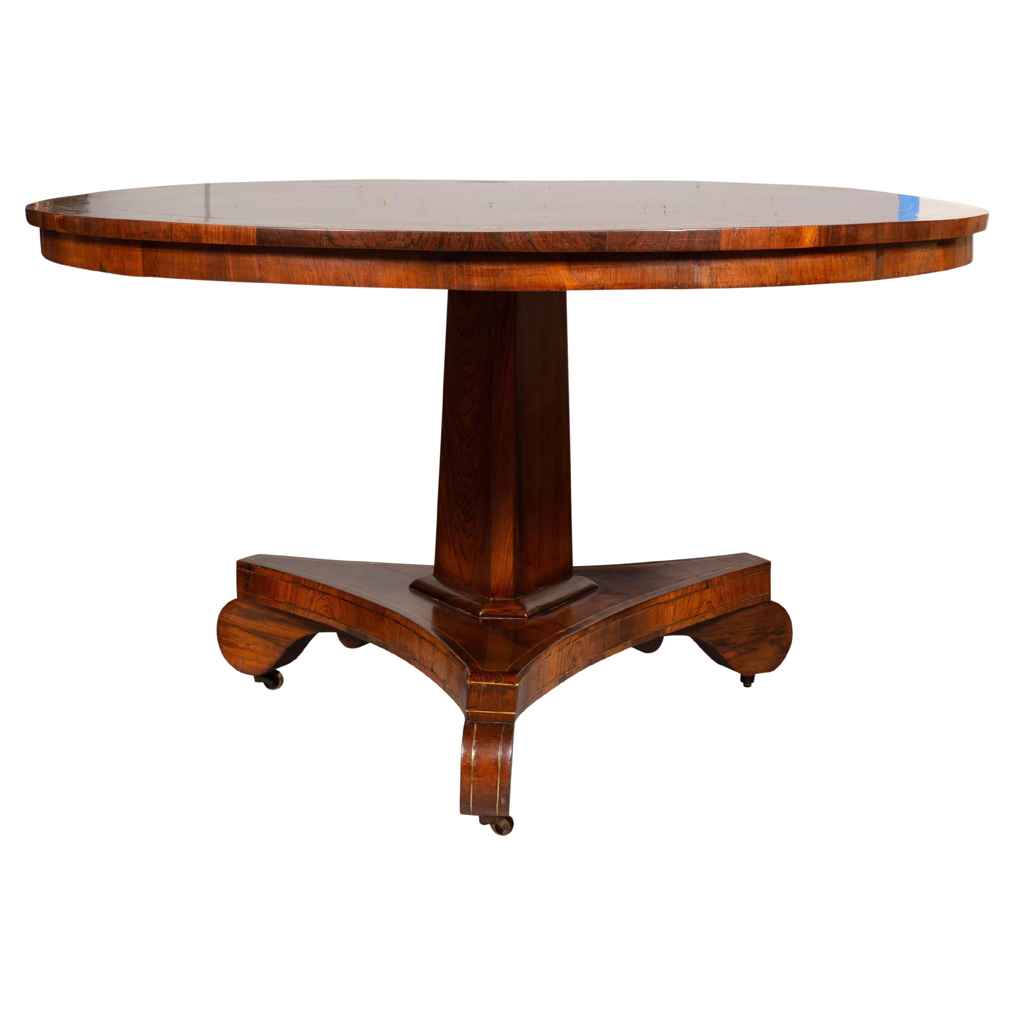 With a circular hinged top with brass inlaid border supported on a triangular support ending on a conforming base with brass stringing and raised on plain Greek form feet. Casters.