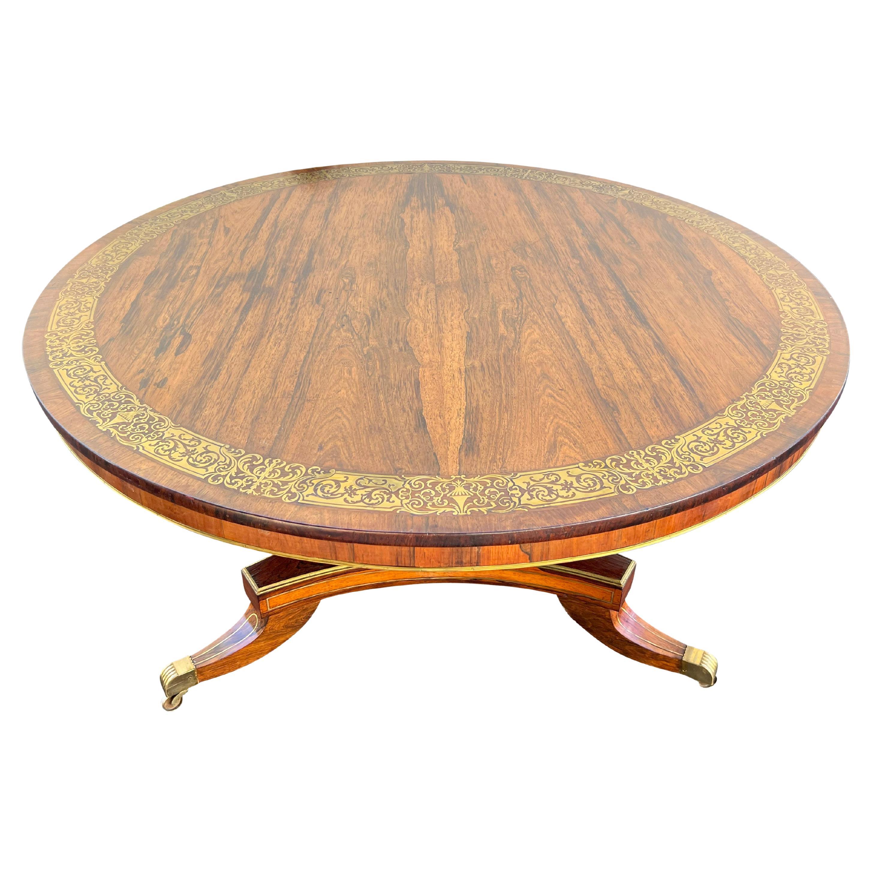 Circular tiltable top with brass inlaid banding with conforming apron on a flat sided brass 
mounted columnar support joining a brass mounted tripartite plinth base raised on three saber legs with brass casters.