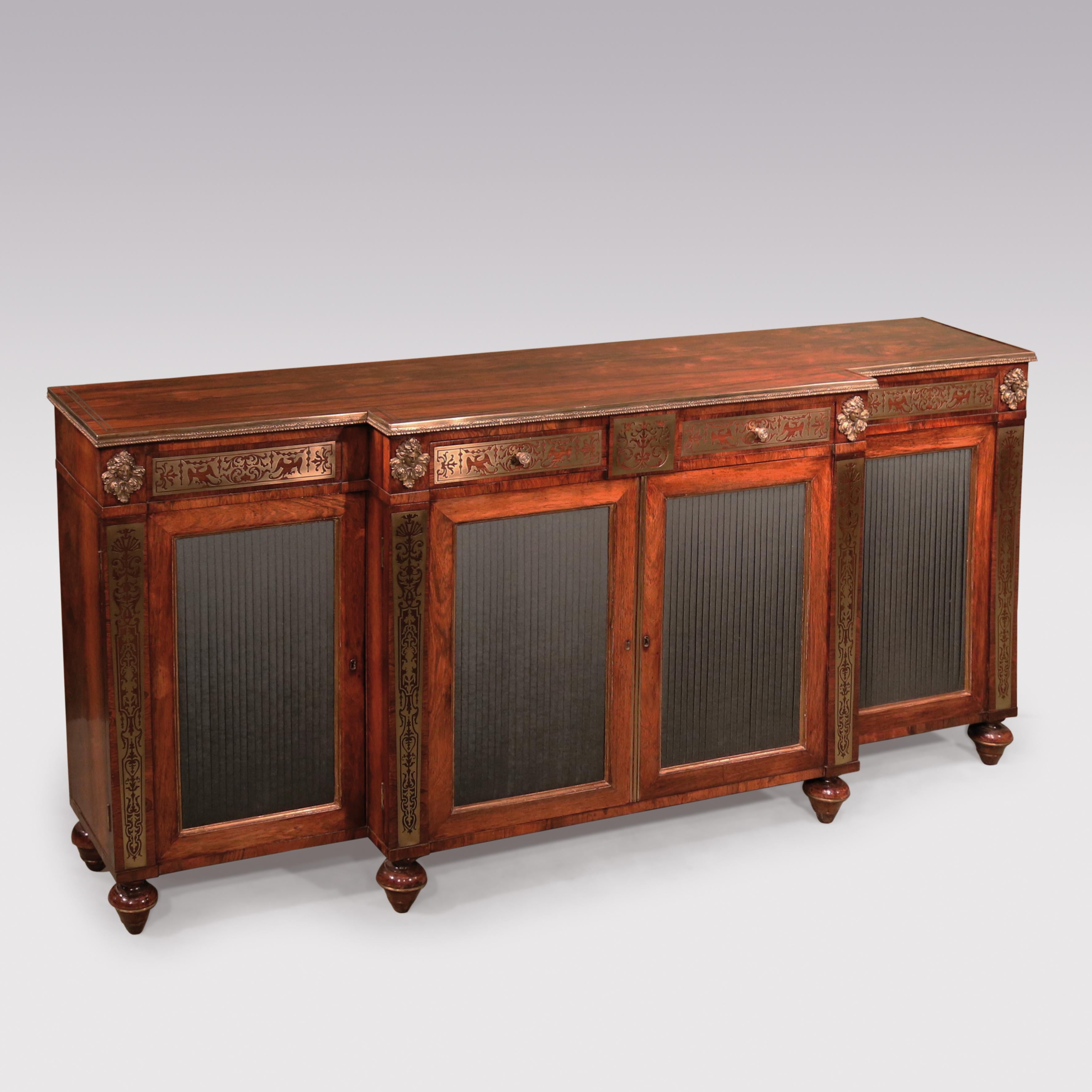 An important early 19th century Regency period rosewood and brass inlaid breakfront chiffonier, with a gilt brass edged top and frieze drawers with inlaid swag and phoenix panels, flanked by gilt brass female heads. The chiffonier having four silk
