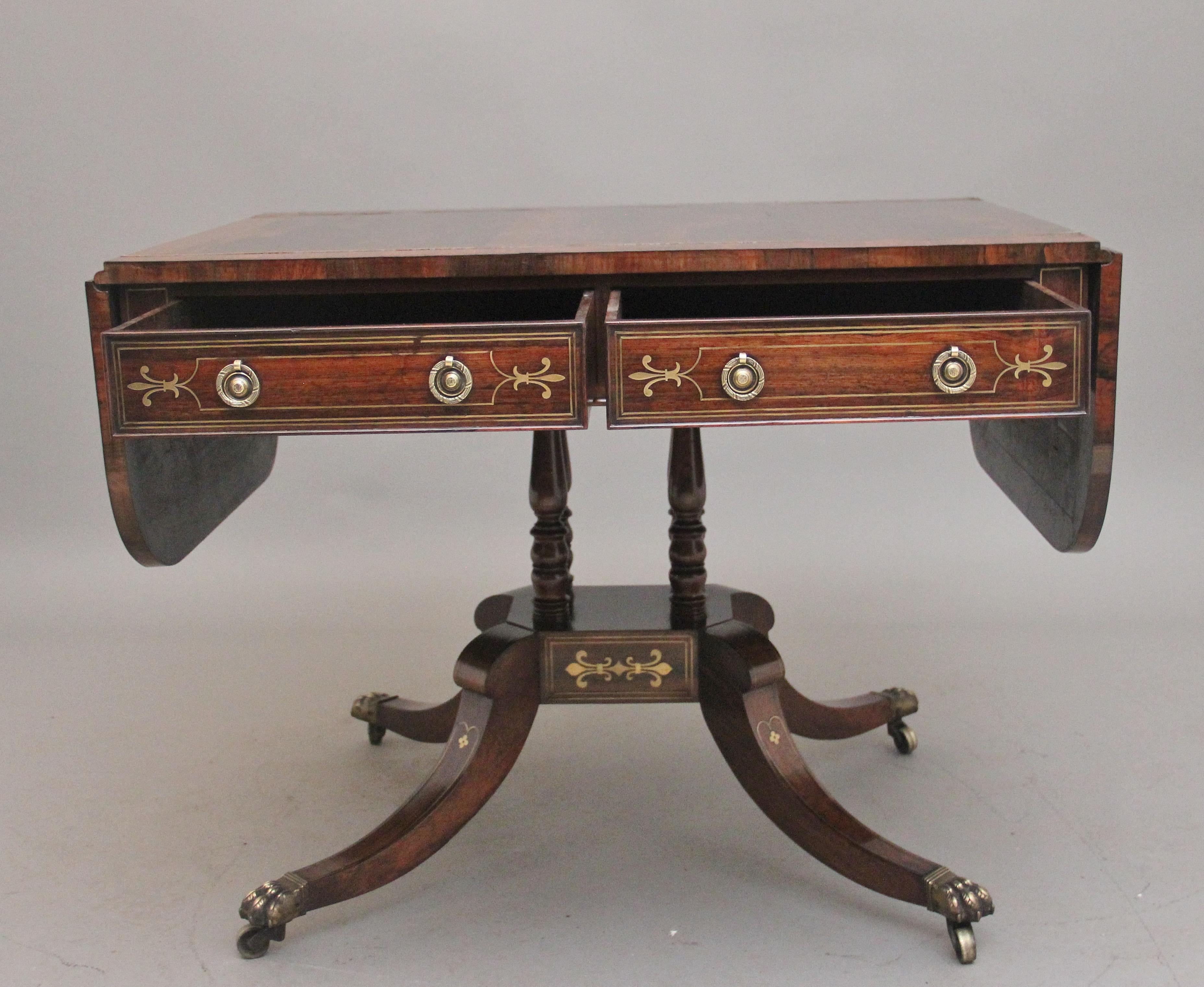 A superb quality early 19th Century rosewood and brass inlaid sofa table, having a wonderfully figured top, crossbanded and having decorative brass inlay, the drop leaves either side lifting up to extend the table, two mahogany lined drawers below