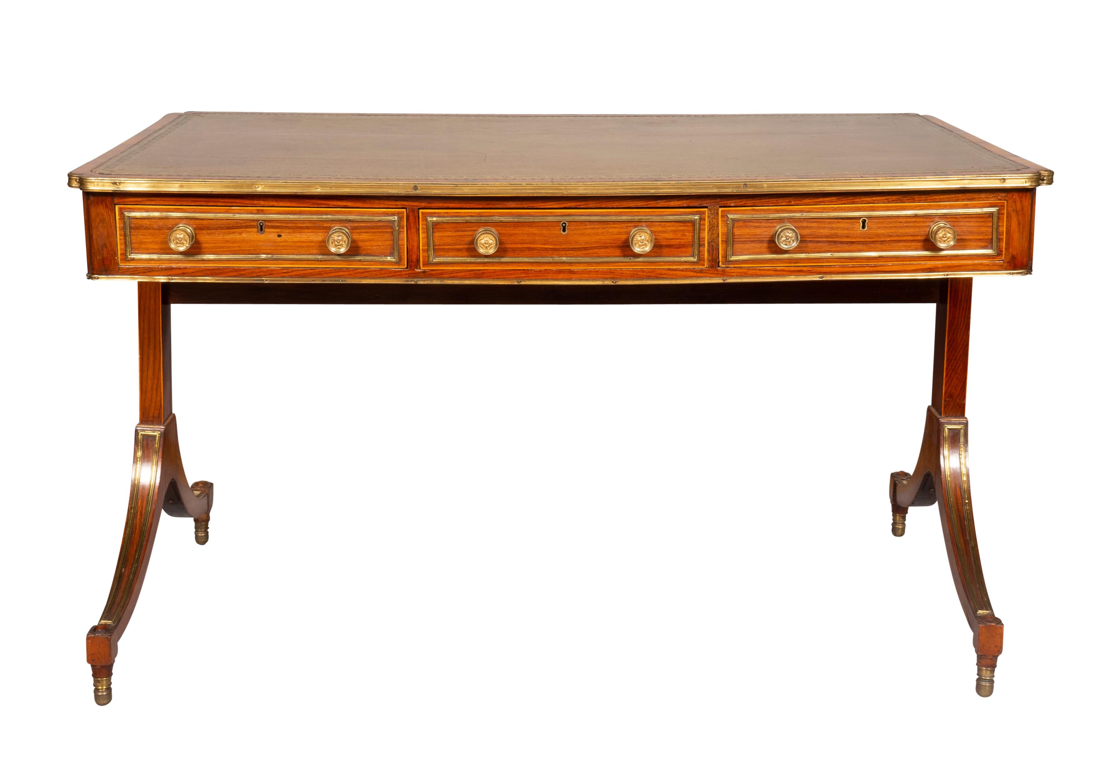 With a rectangular top with inset brown leather top with gold tooling. The edge of the top with pinched corners and molded brass edge. The frieze with three drawers and three opposing false drawers, the sides with false drawers, raised on a trestle