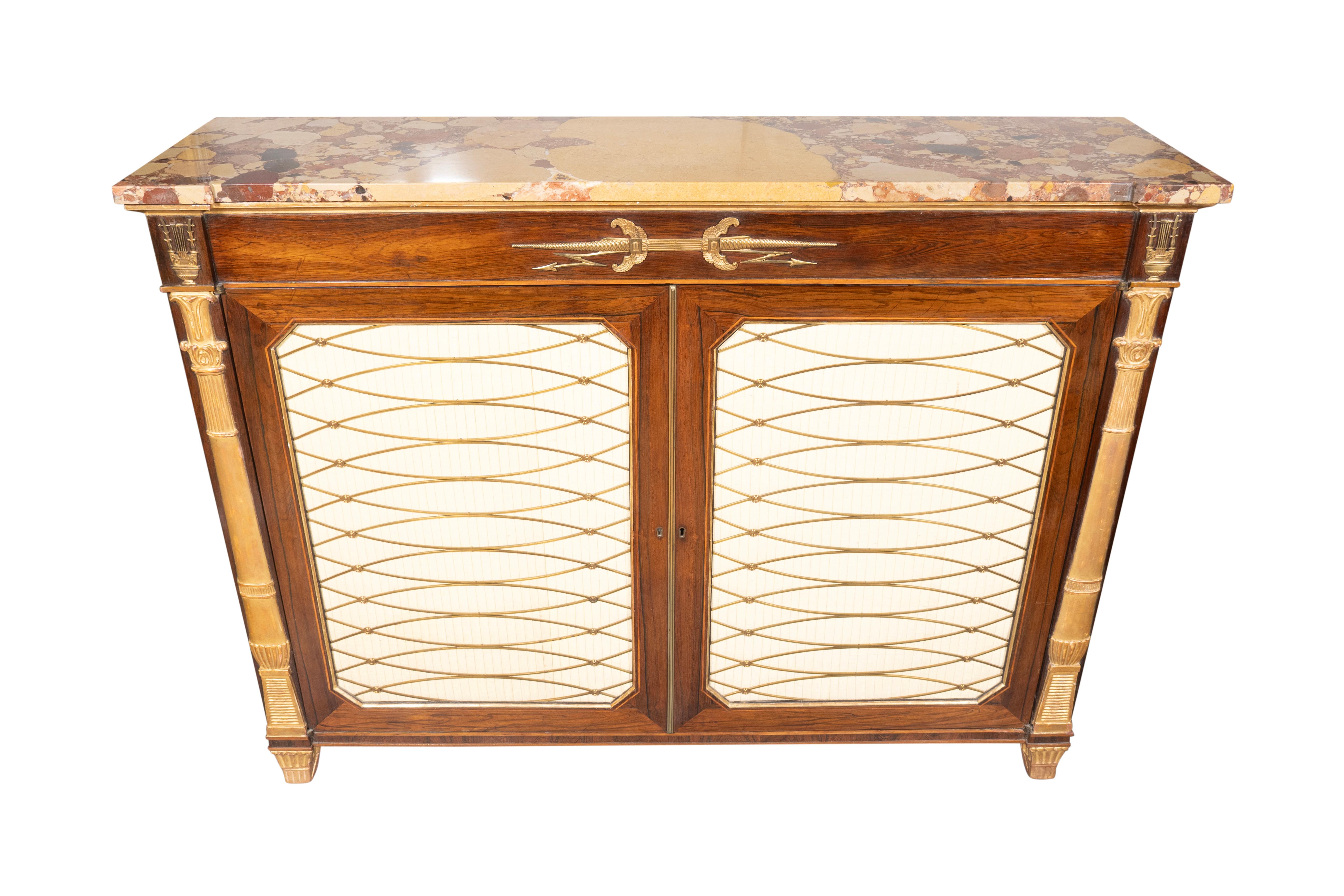 With a likely replaced breche de alep marble top of breakfront form over a frieze with musical bronze mounts. A pair of cabinet brass grill doors enclosing shelves flanked by giltwood columns. Saber form gilt wood feet.