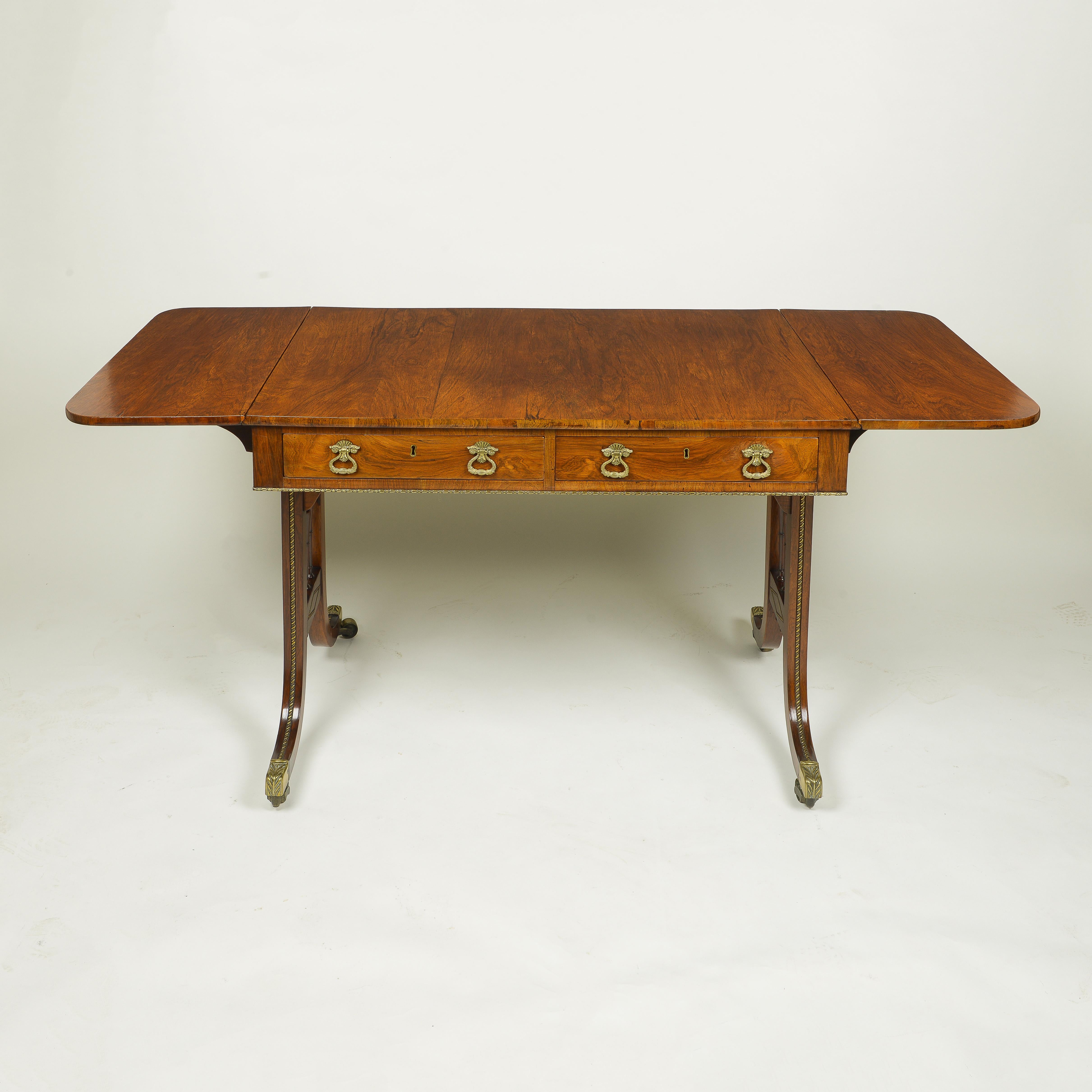 The rectangular top with rounded drop-ends, fitted with two frieze drawers with drop handles; raised on ring-turned end supports inlaid with bead-and-reel gilt-metal banding, terminating in foliate-cast caps and casters. 

Measures : Width: 37.75