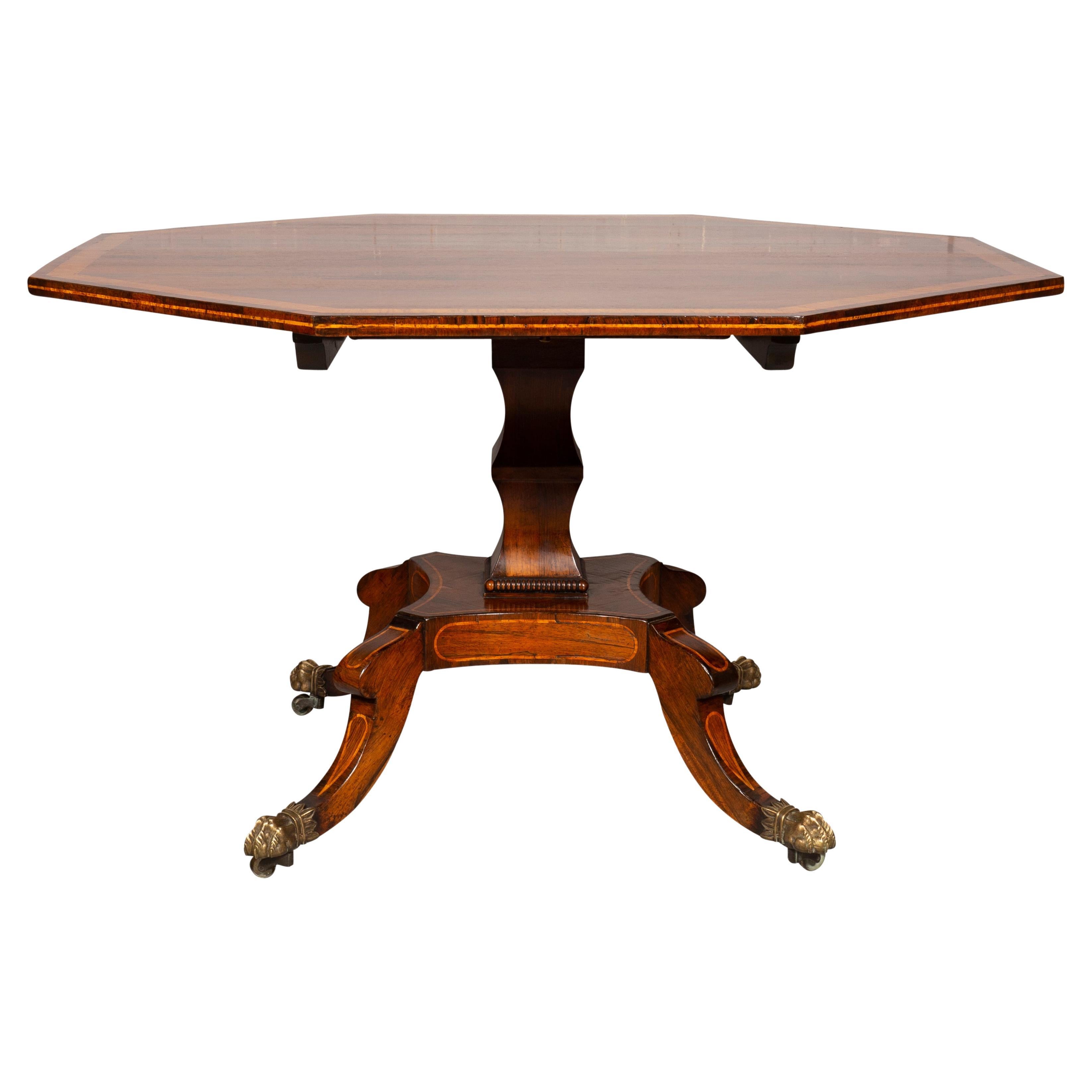 Octagonal top with satinwood banding , hinged to tilt , raised on a shaped support joining a platform with four saber legs with stringing inlay and paneled inlays and lions paw brass feet and casters. Provenance ; Beverly Hills Collection.