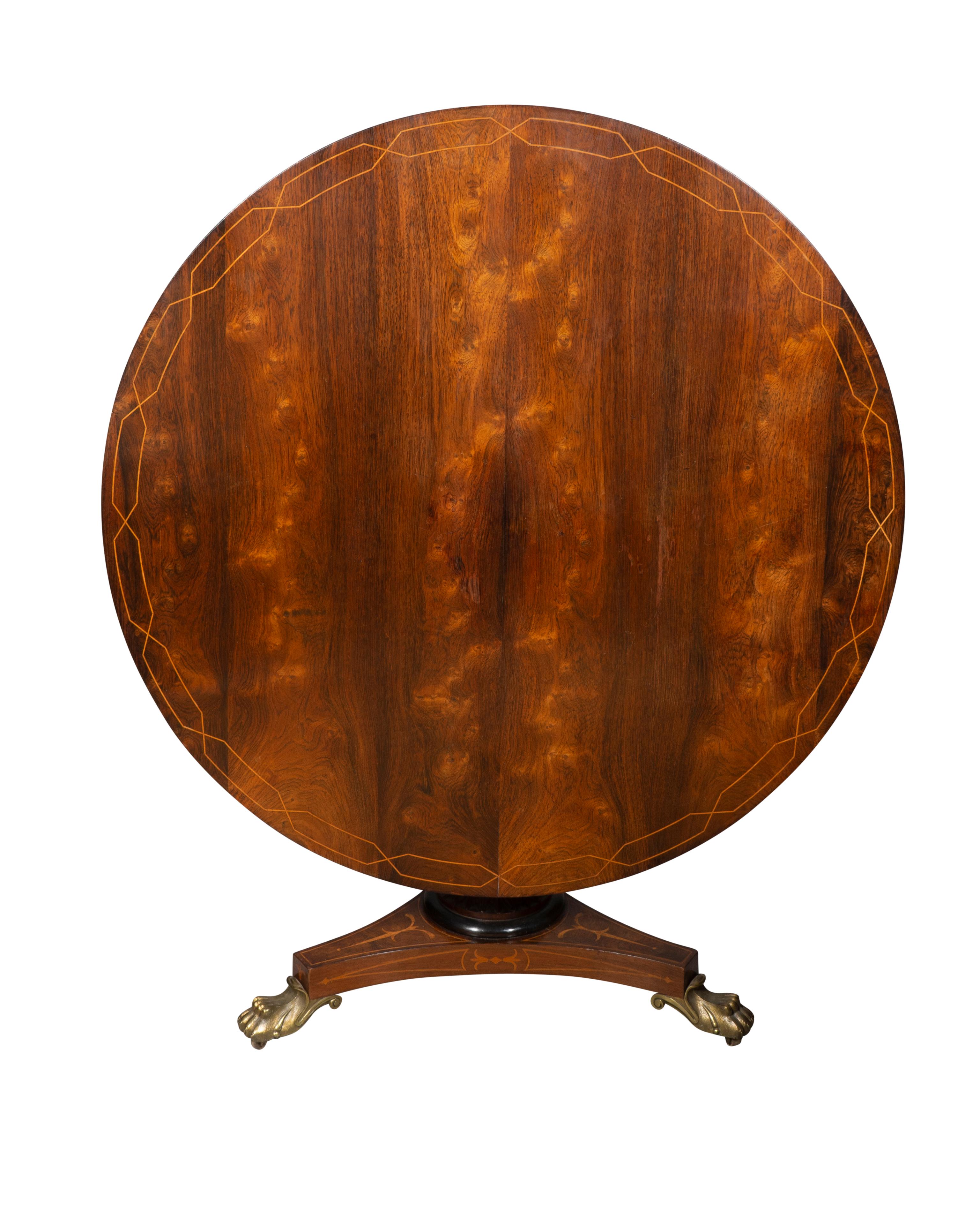 Hinged circular top with geometric satinwood inlaid border and apron. All on a circular spiral carved tapered support joining a tripartite inlaid plinth base with brass paw feet.