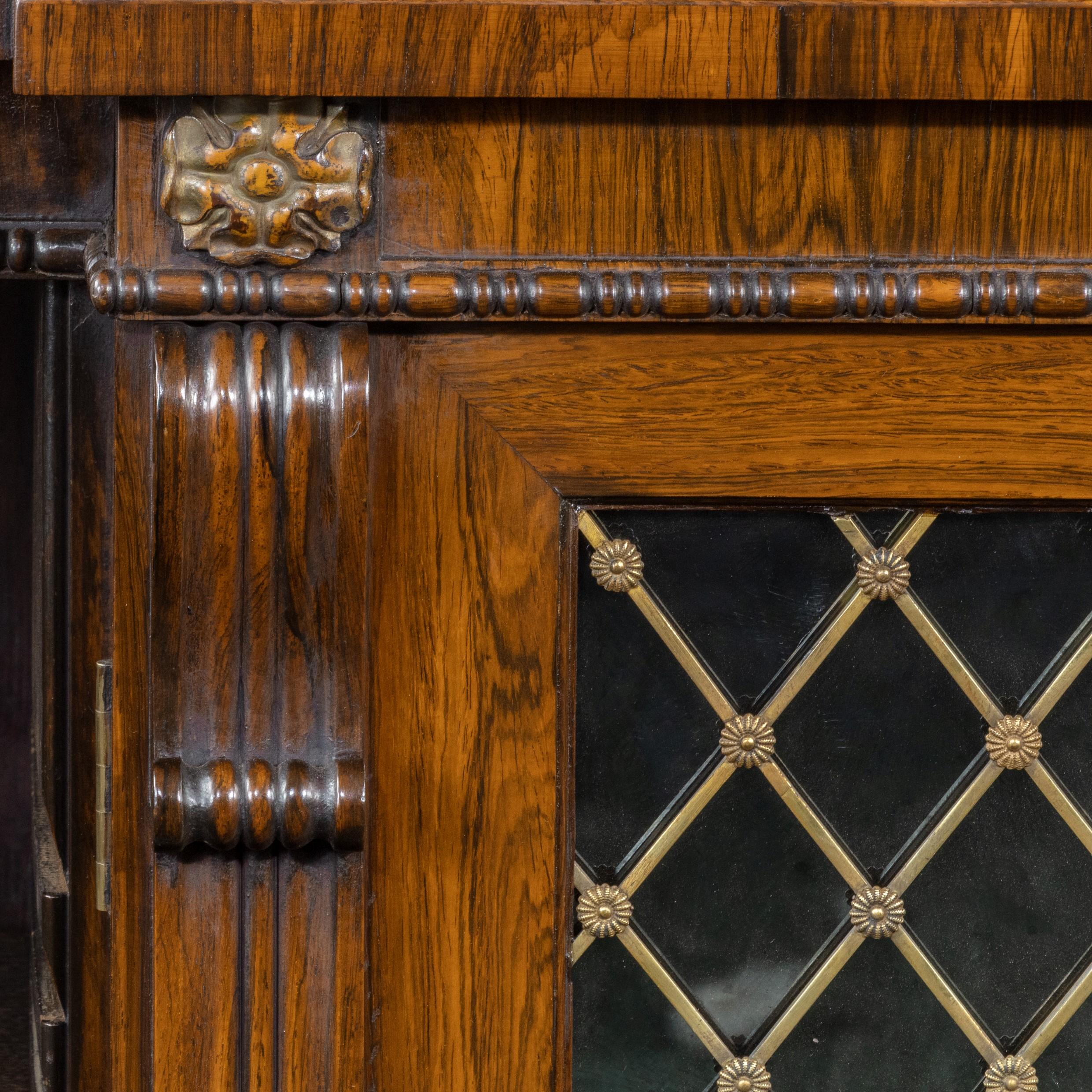 A large Regency rosewood breakfront side cabinet/open bookcase, attributed to Gillows, of long rectangular form with two central glazed cupboard doors flanked by open bookcases, each enclosing two adjustable shelves, retaining the original brass